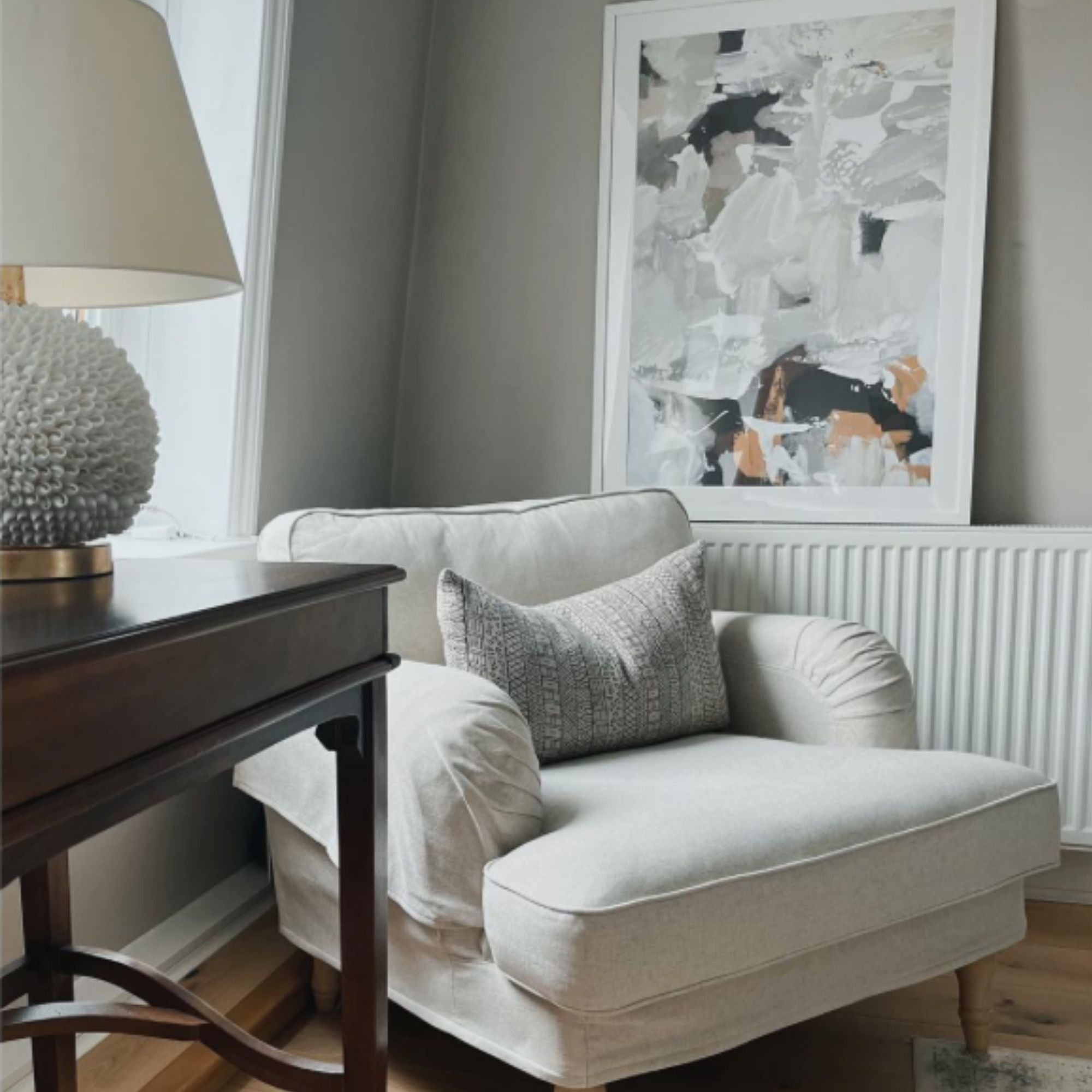framed abstract art in grey with a hint of gold by arm chair above radiator