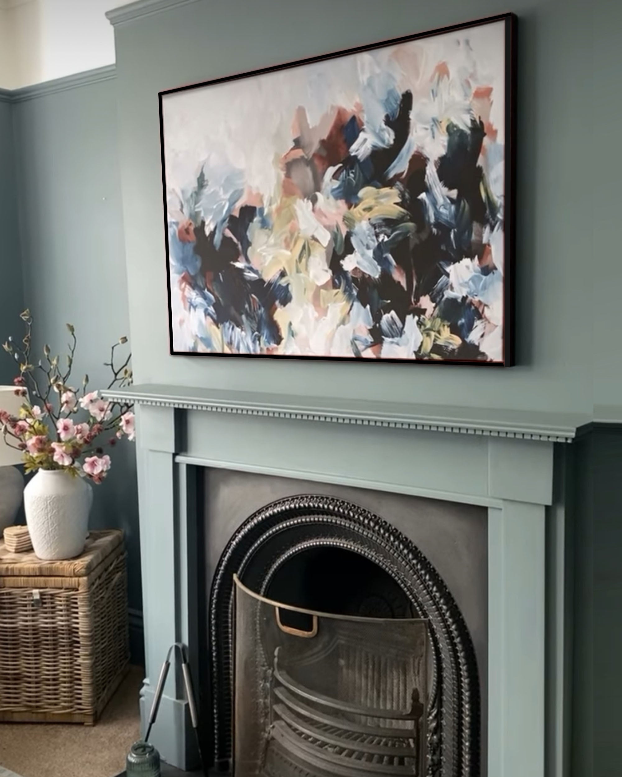 Abstract painting above a fireplace with a vase of flowers on a side table.