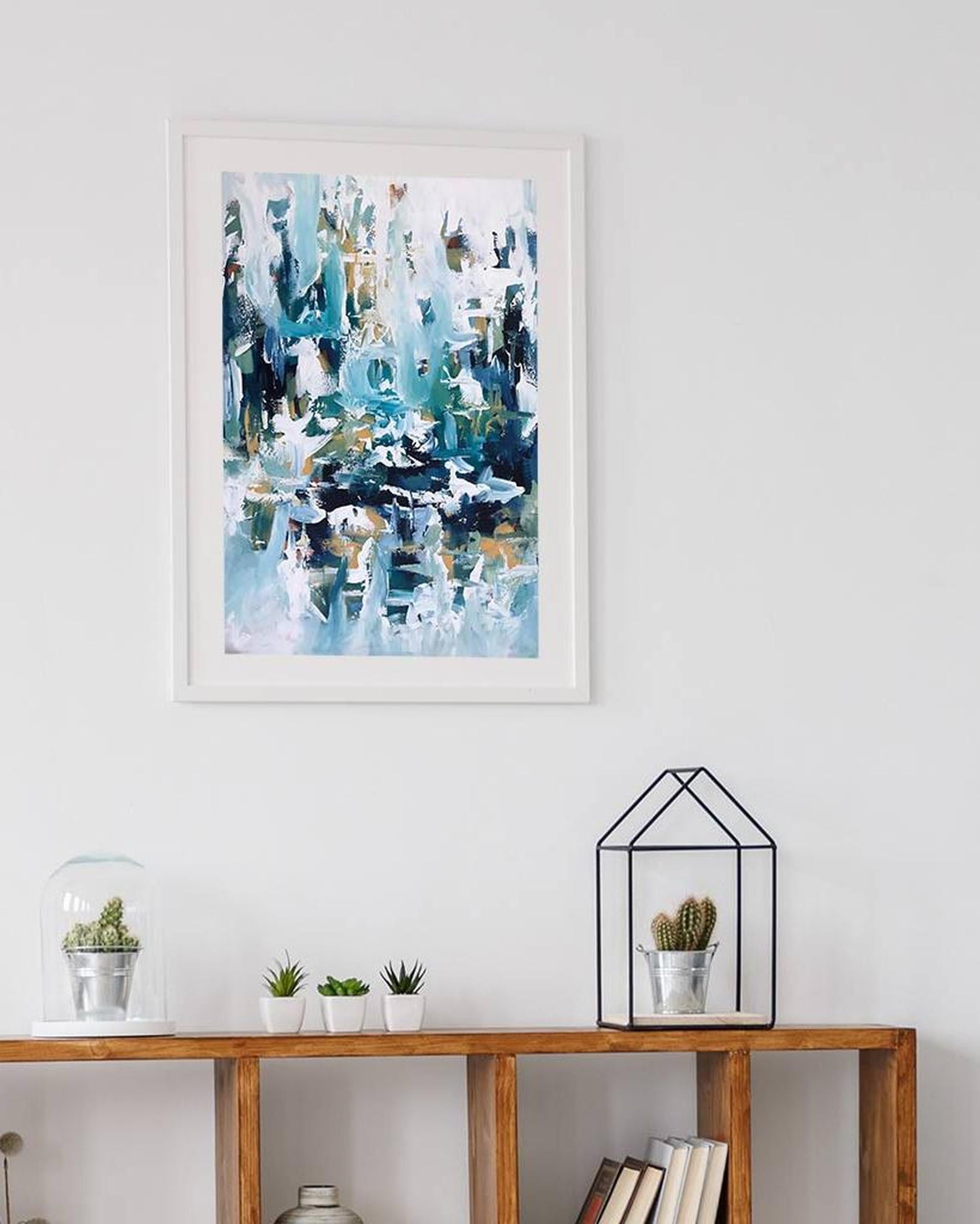 Framed abstract art piece on a wall above a wooden console table with decorative items.