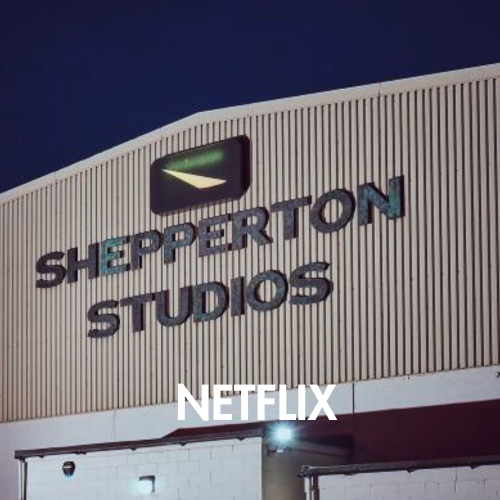 Shepparton Studios building exterior at night with large raised 'SHEPPERTON STUDIOS' lettering and a Netflix logo/text overlay near the bottom.
