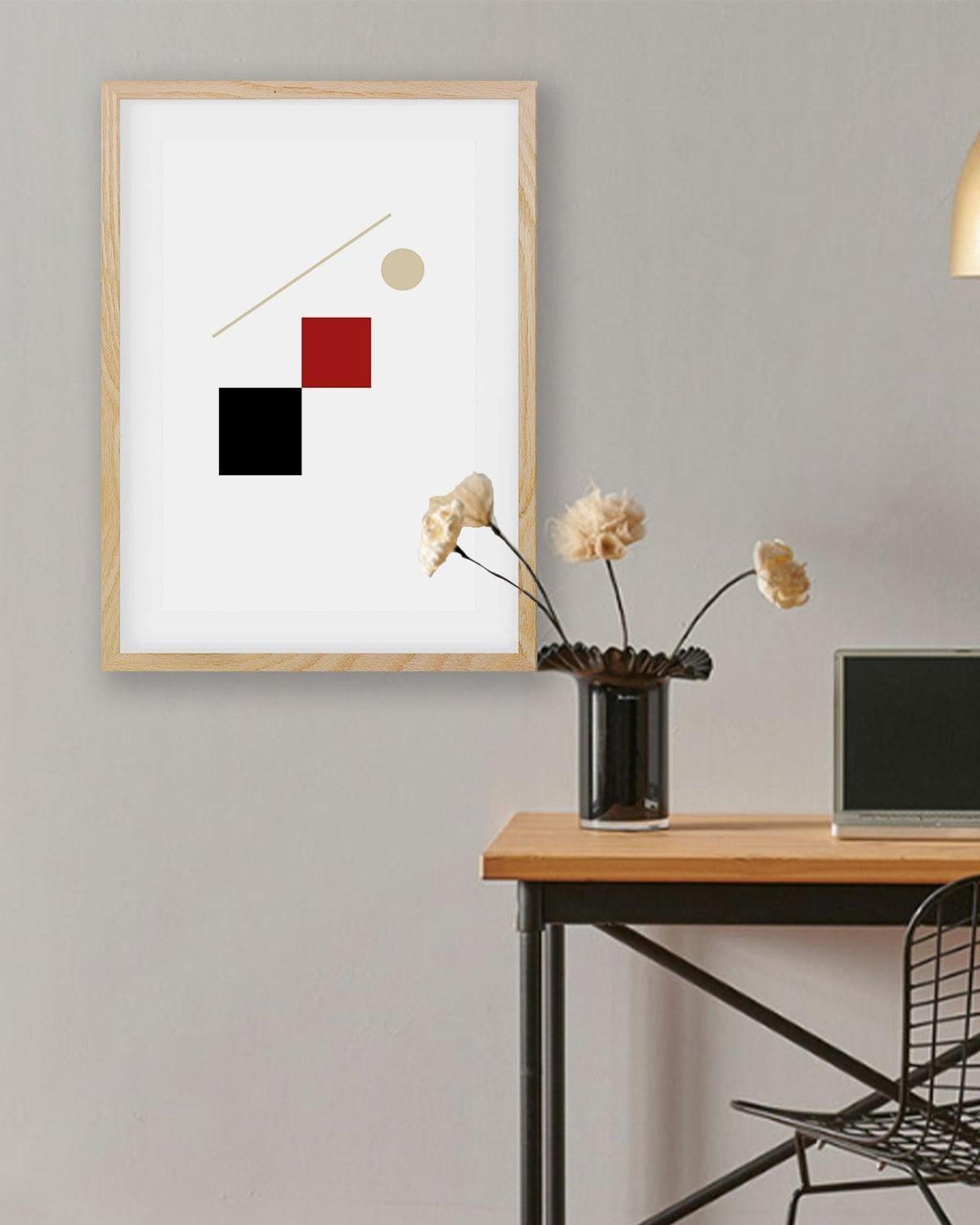 Abstract art print with geometric shapes on a wall above a desk.