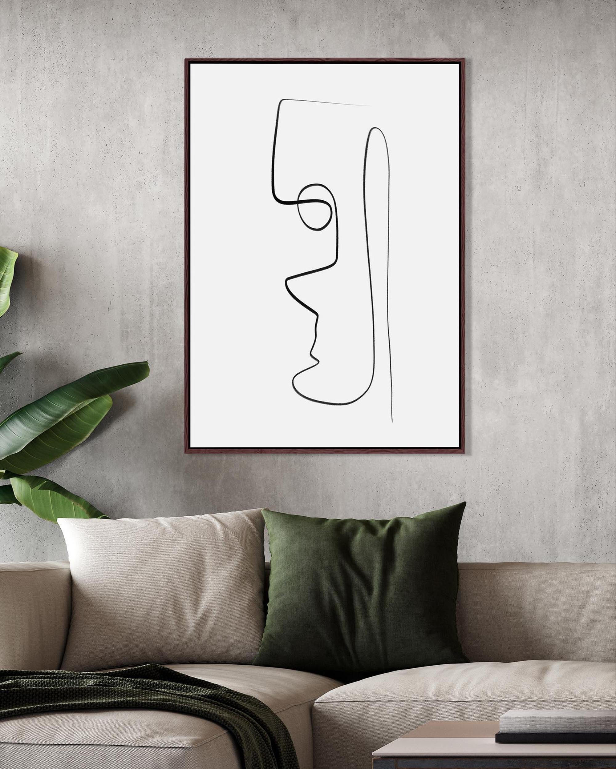 Abstract line art of a face on a wall above a sofa with green cushions.