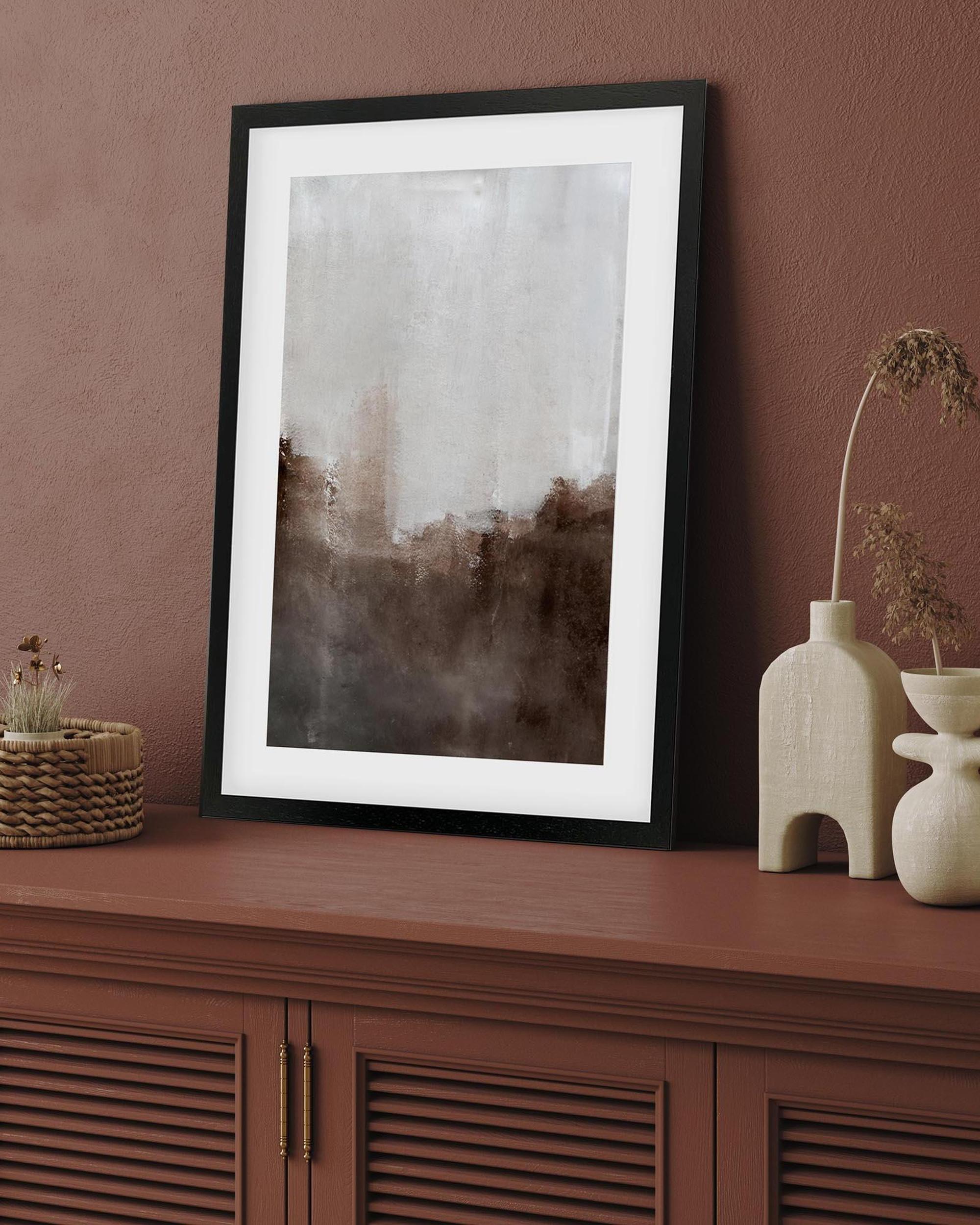 Framed abstract art piece on a wooden cabinet with decorative items.
