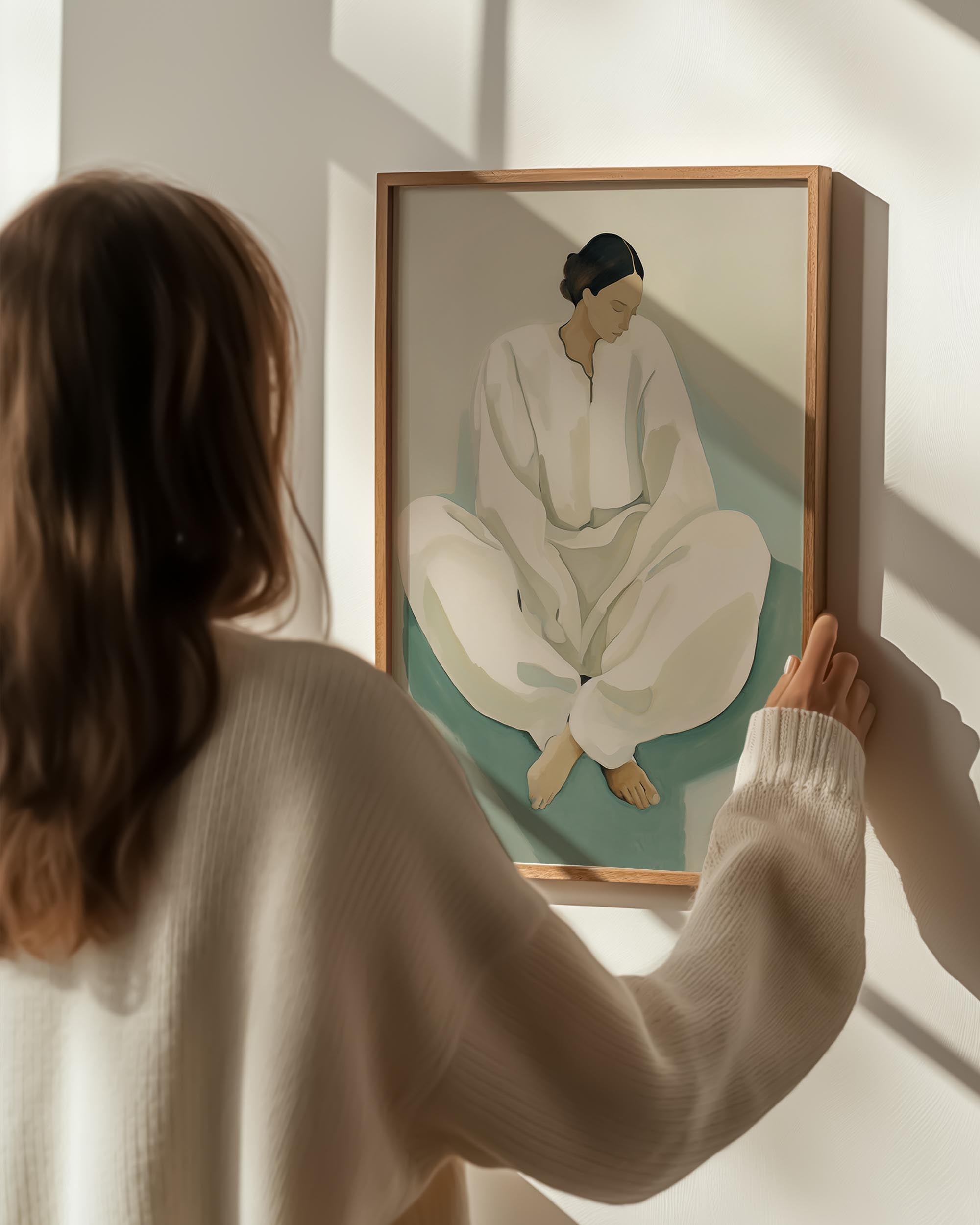 Person holding a framed painting of a person in a white outfit against a light wall.