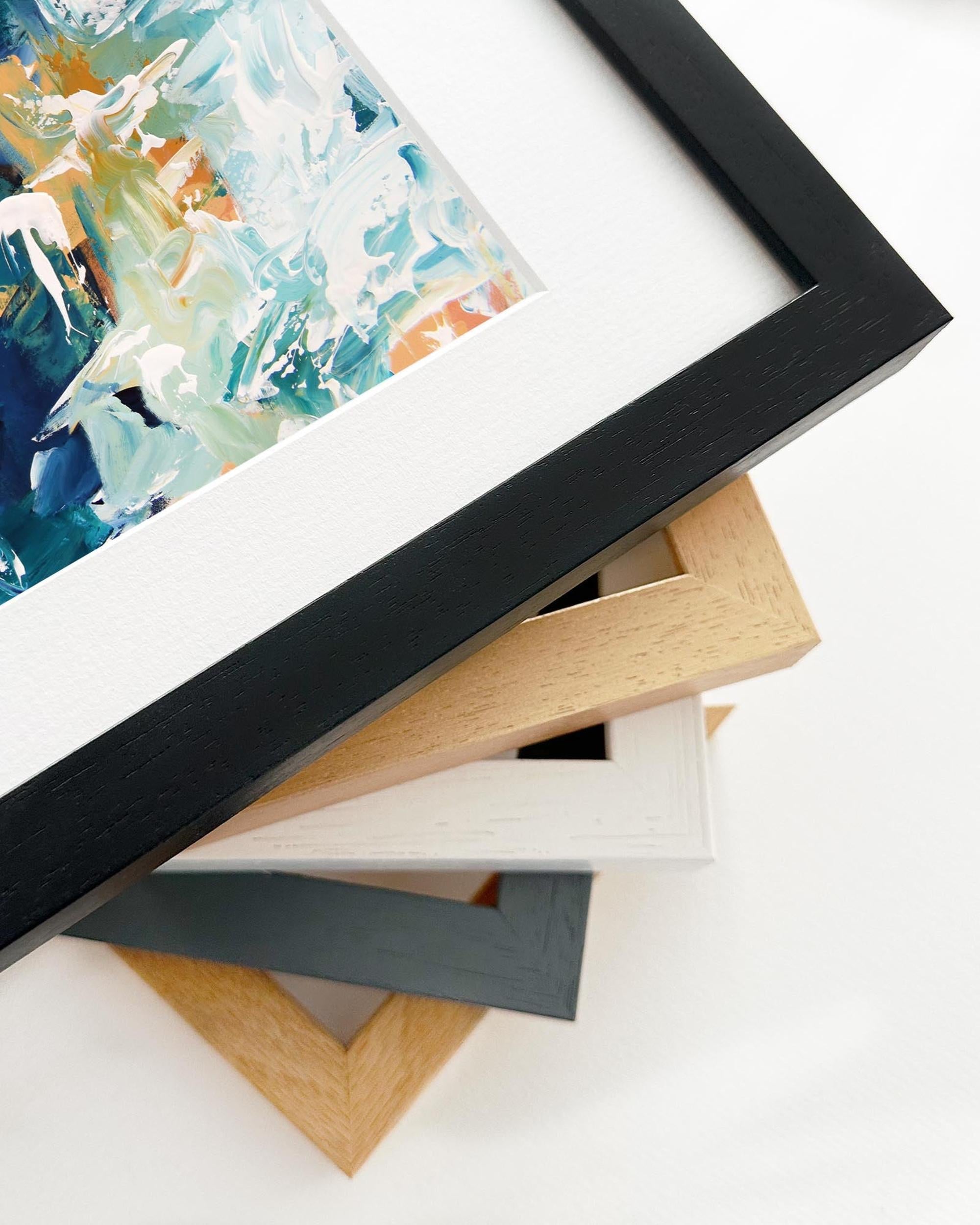 Stack of variously framed artworks on a white surface