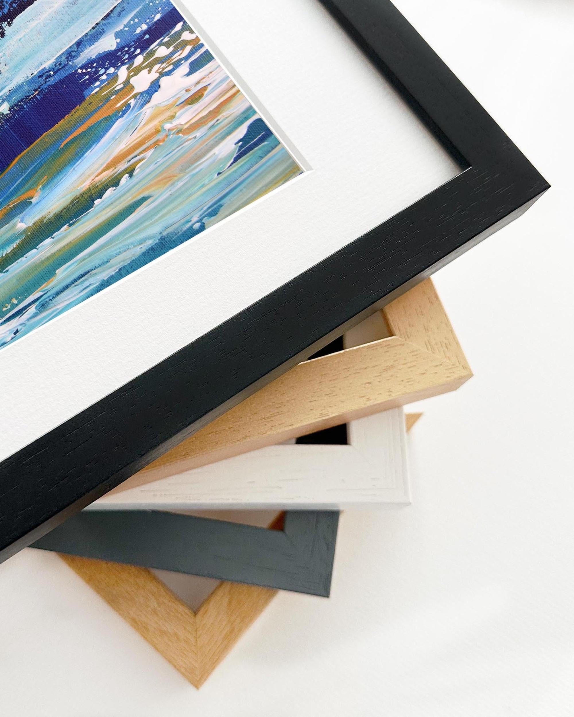 Stack of variously framed artworks on a white surface