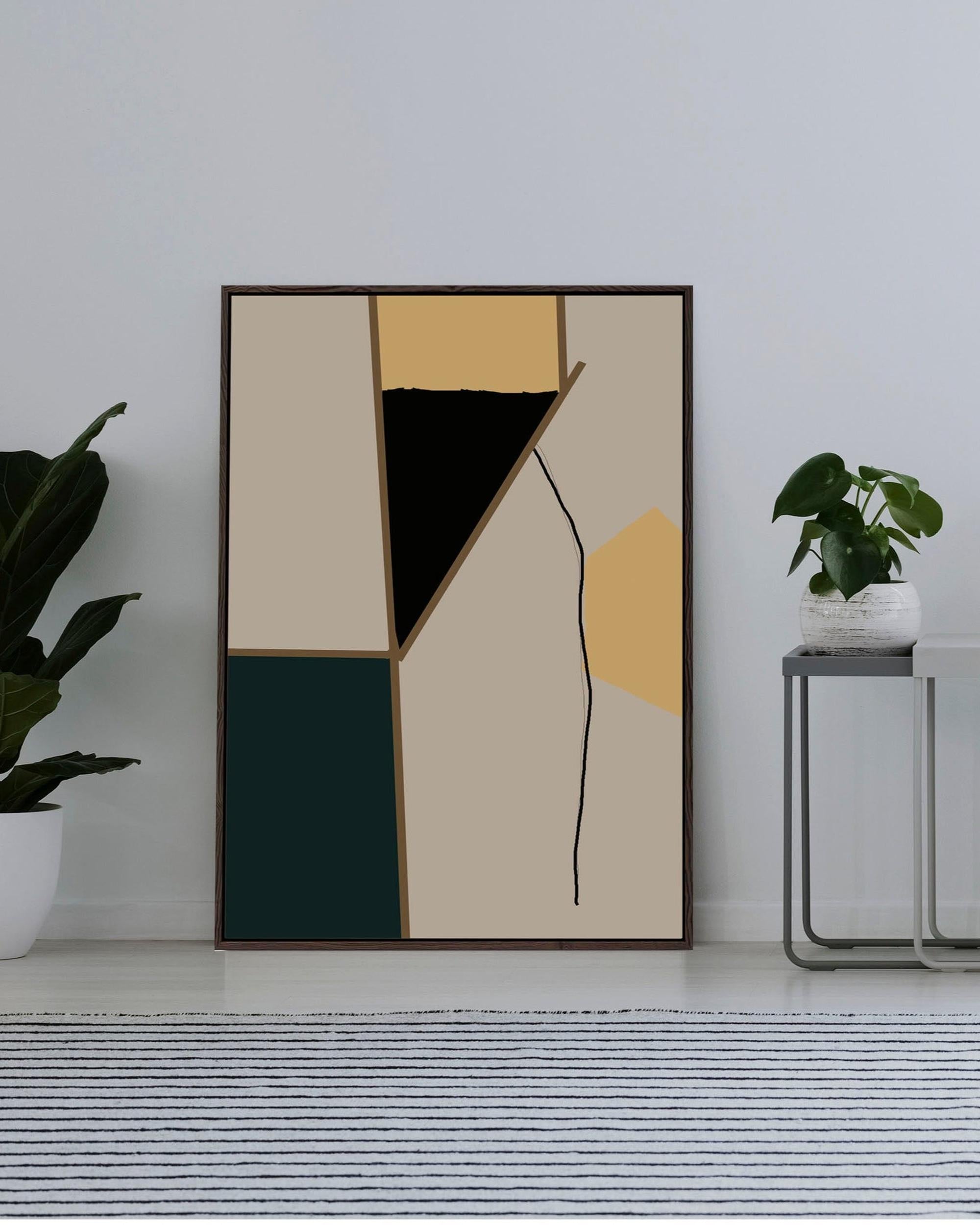 Abstract art print in a black frame on a white wall with plants and a side table.