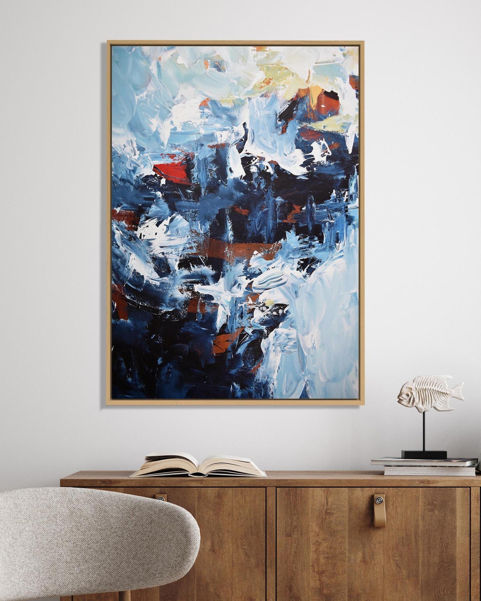 Abstract painting on a wall above a wooden cabinet with books and a chair.