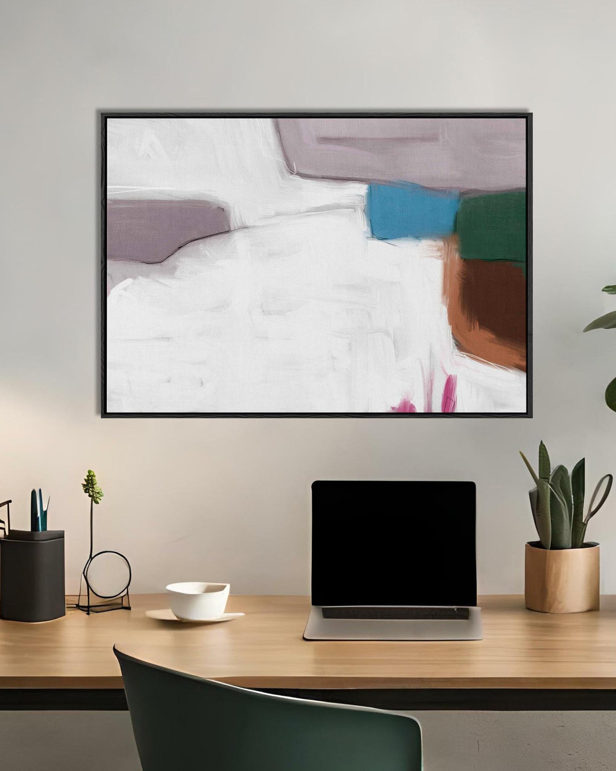 Abstract art piece on a wall above a desk with a laptop and office supplies.