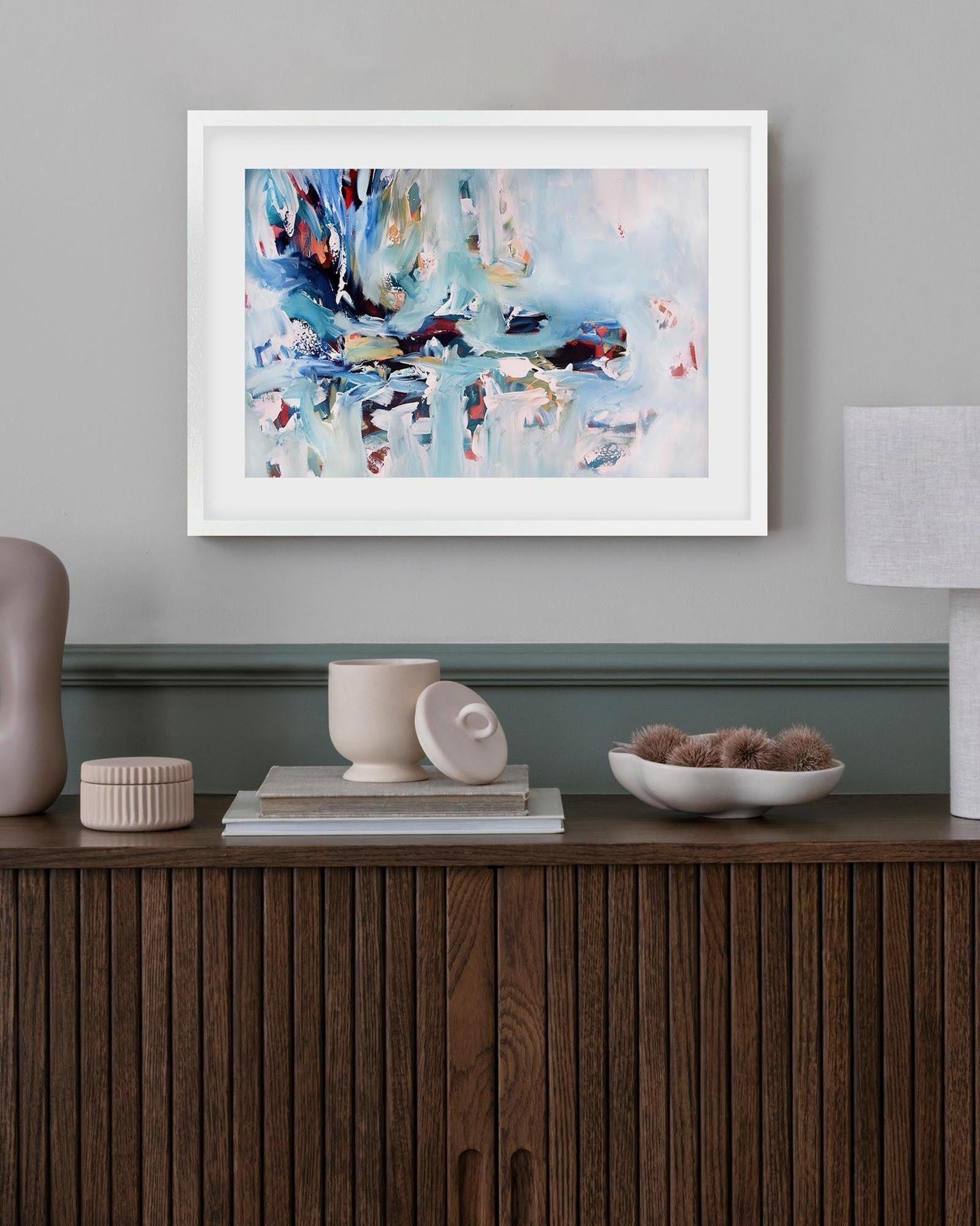 Framed abstract painting on a wall above a wooden console table with decorative items.