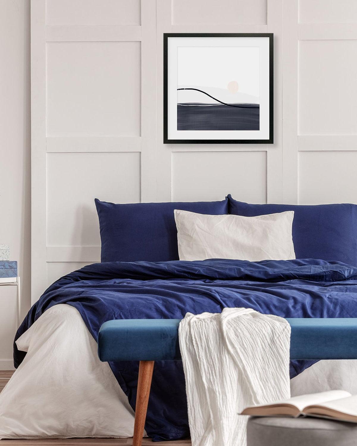 Bedroom with blue bedding, white pillows, and a framed artwork on the wall.