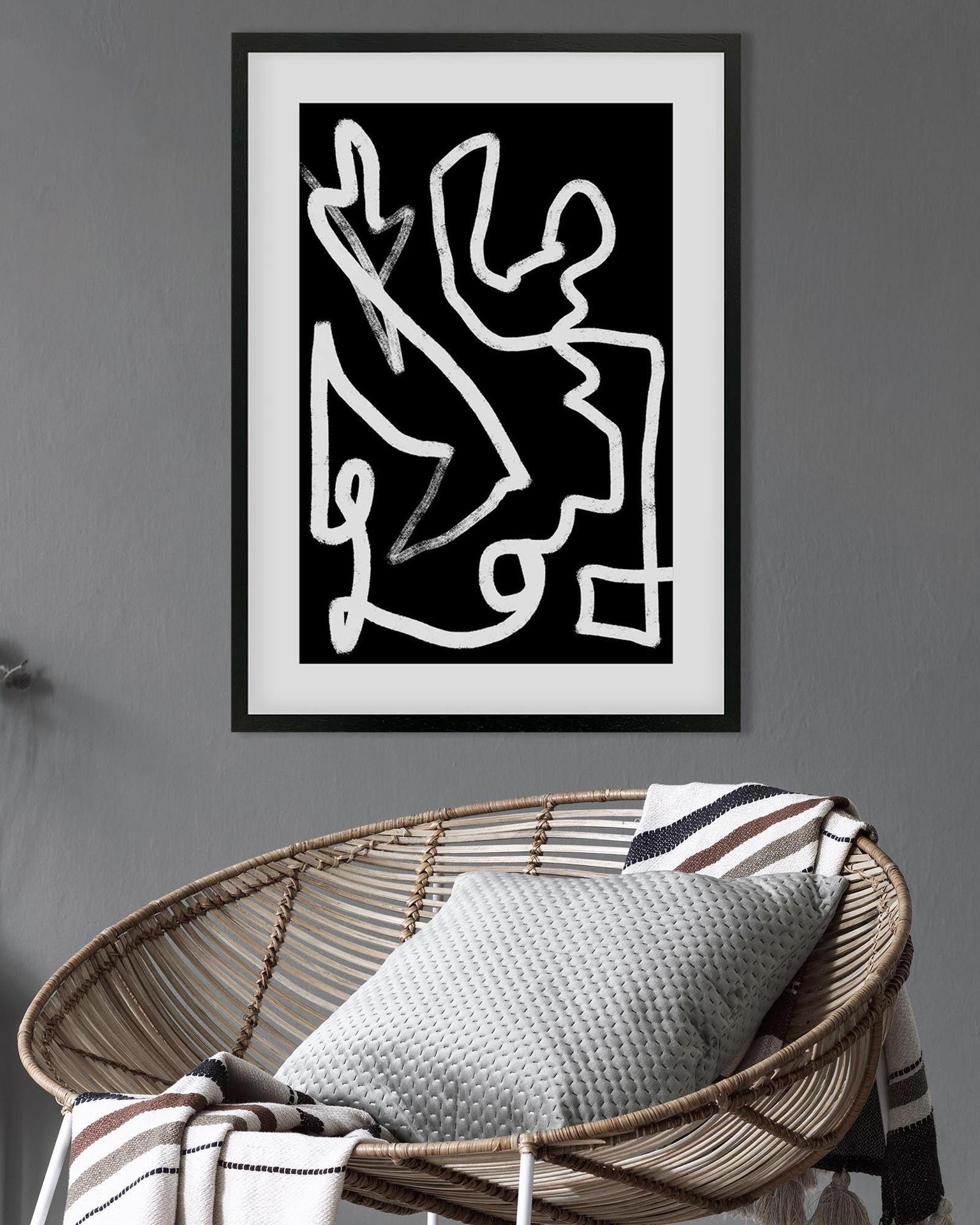 Framed abstract artwork on a gray wall above a wicker chair with a cushion.