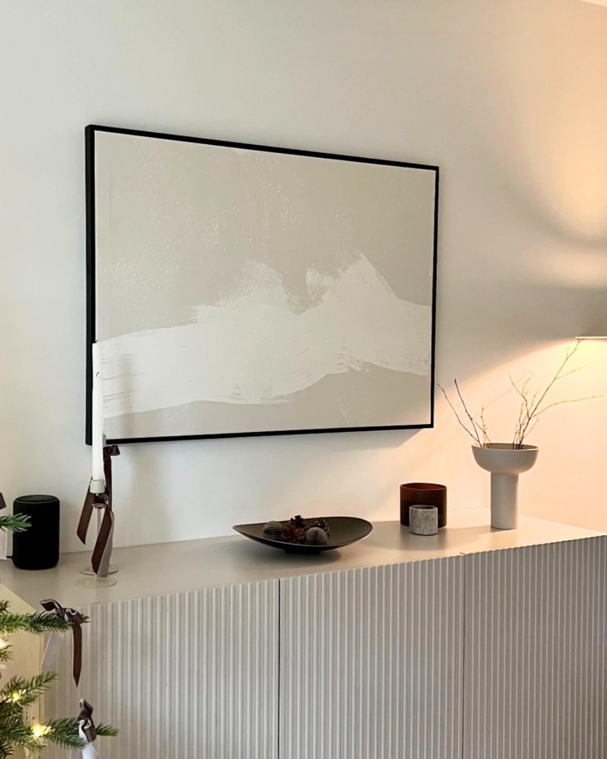 Framed abstract art on a wall above a white cabinet with decorative items.