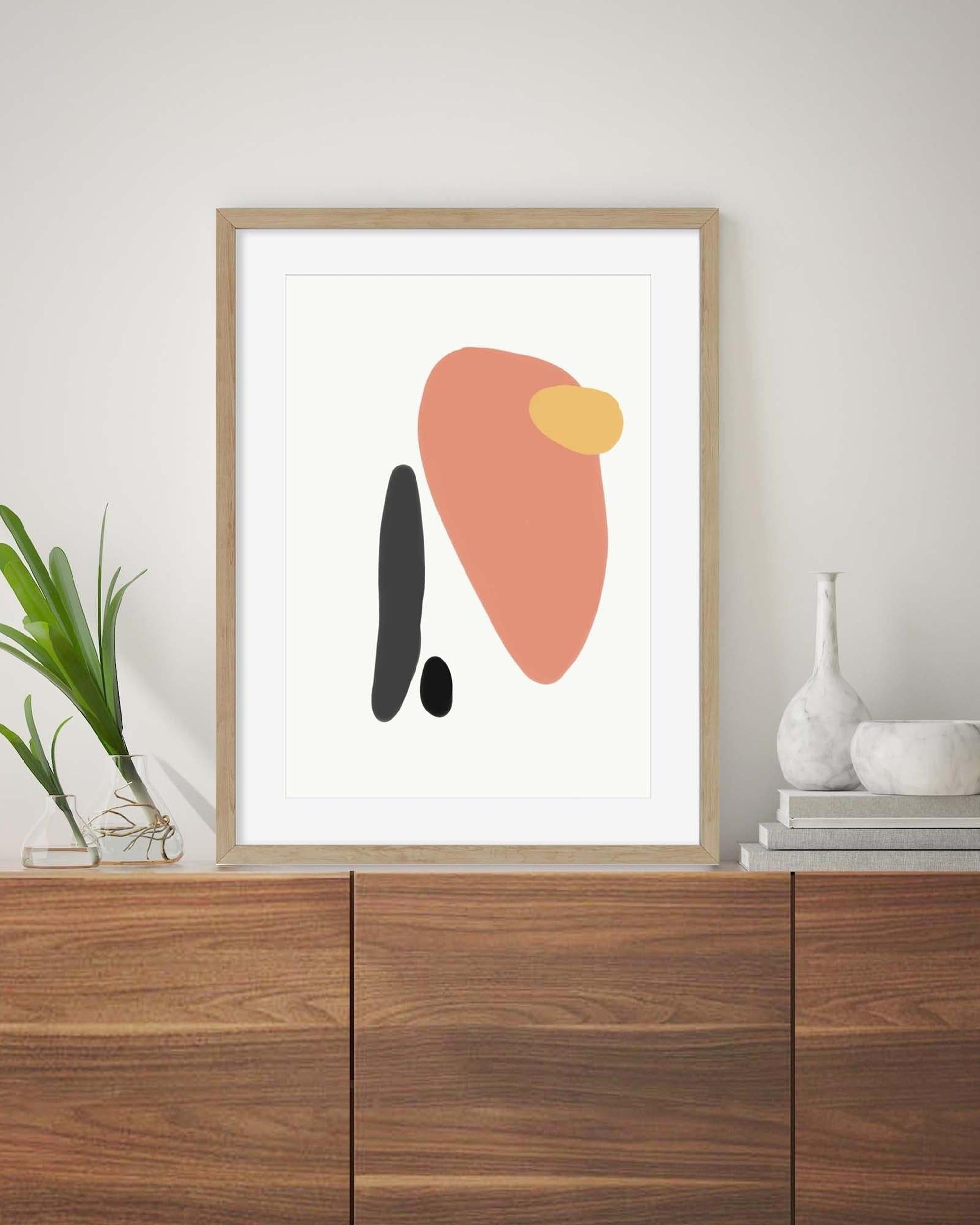 Framed abstract art print with geometric shapes on a wooden shelf.