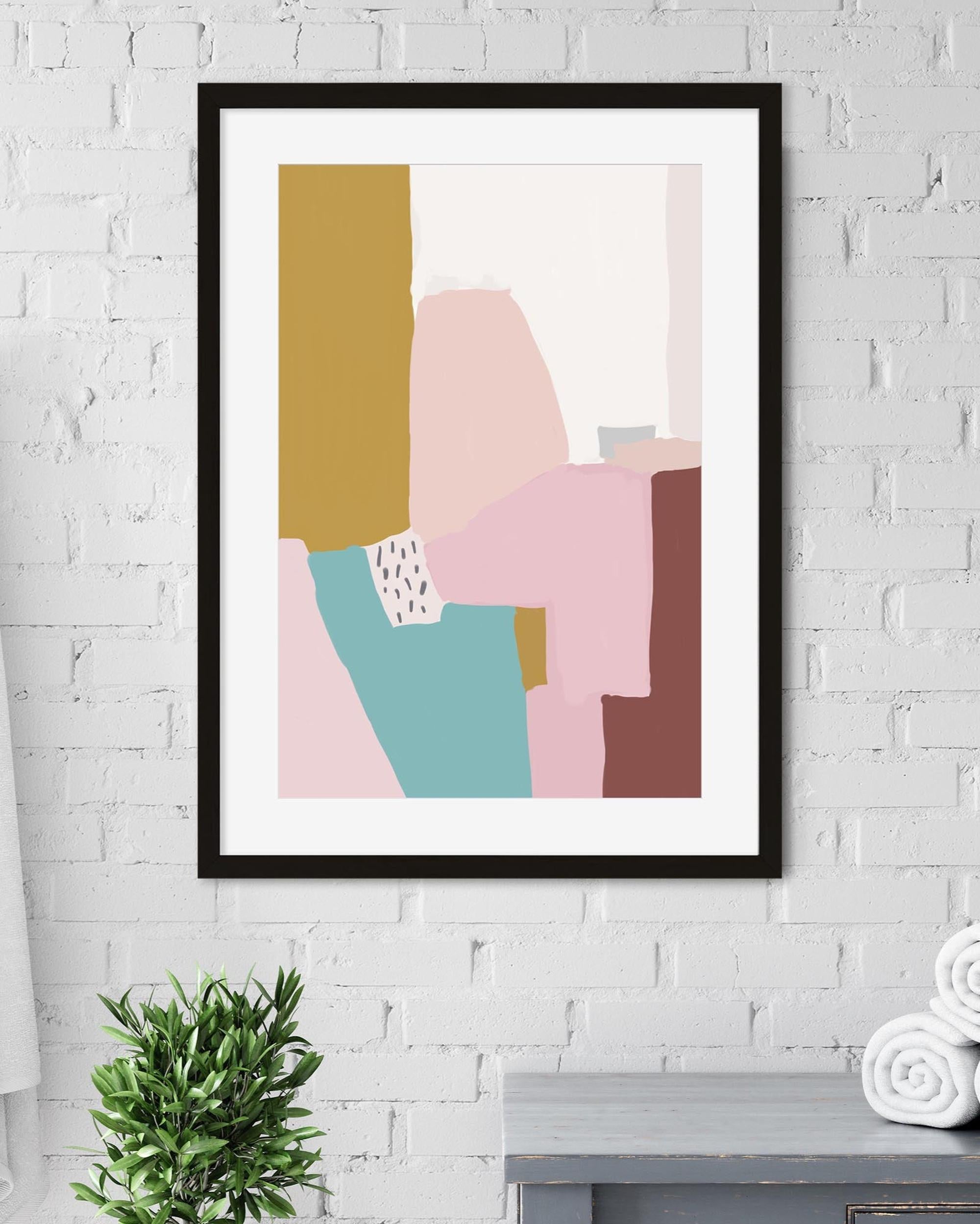 Framed abstract art print with geometric shapes on a white brick wall.