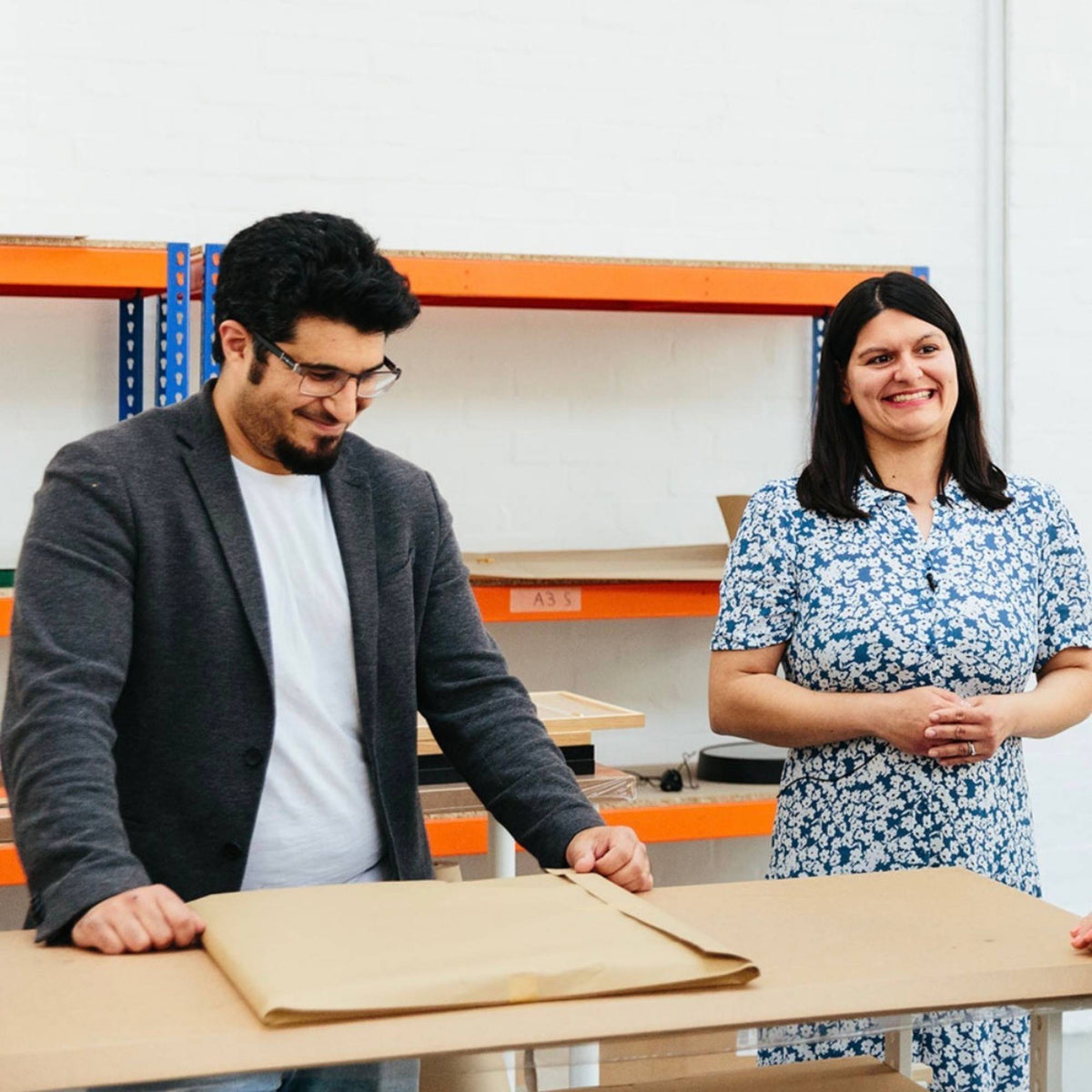 Two people artist Omar Obaid and Summer Obaid working together in a warehouse setting with shelves and cardboard boxes at Abstract House studio London