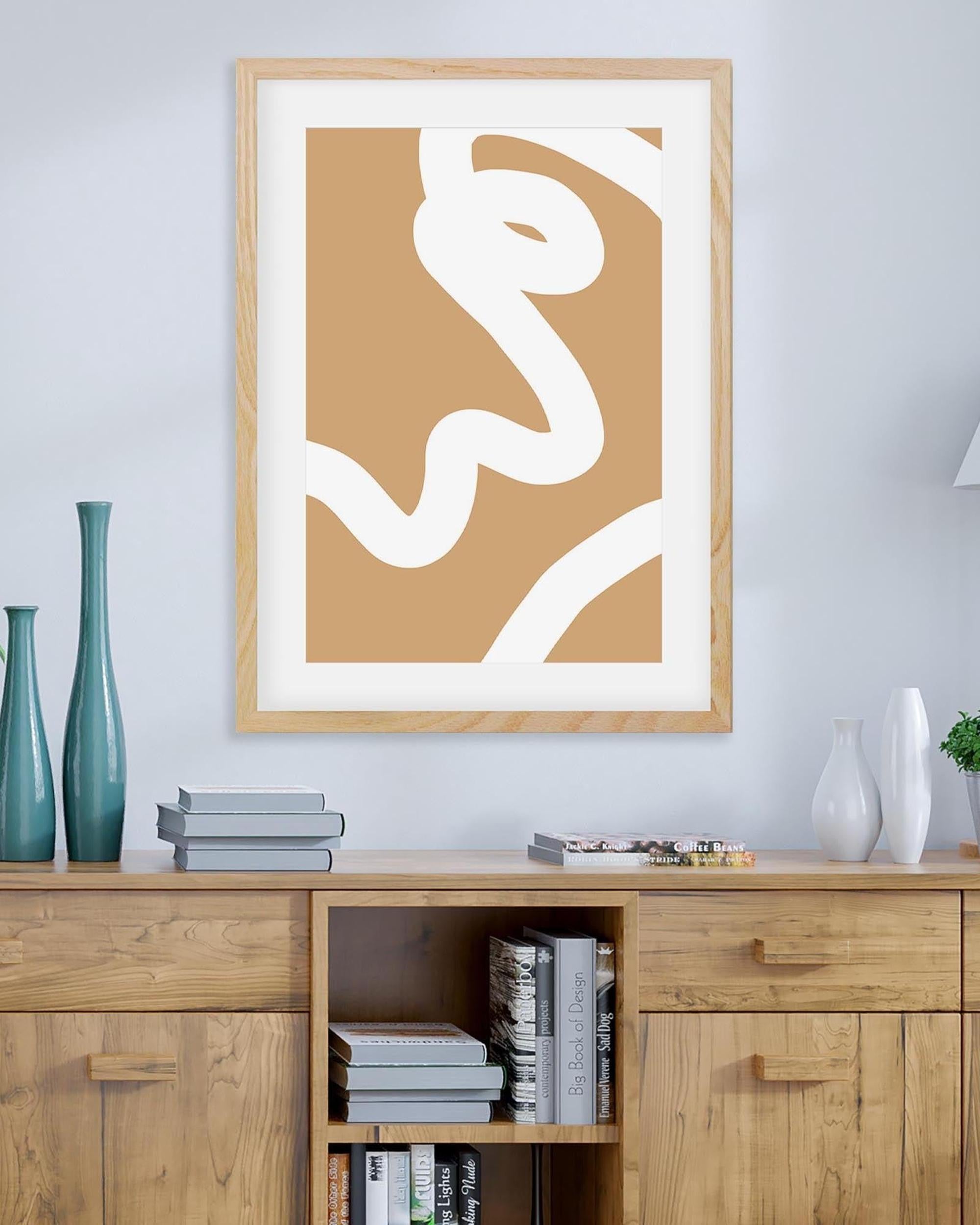 Abstract art print in a wooden frame on a wall above a wooden cabinet with books.