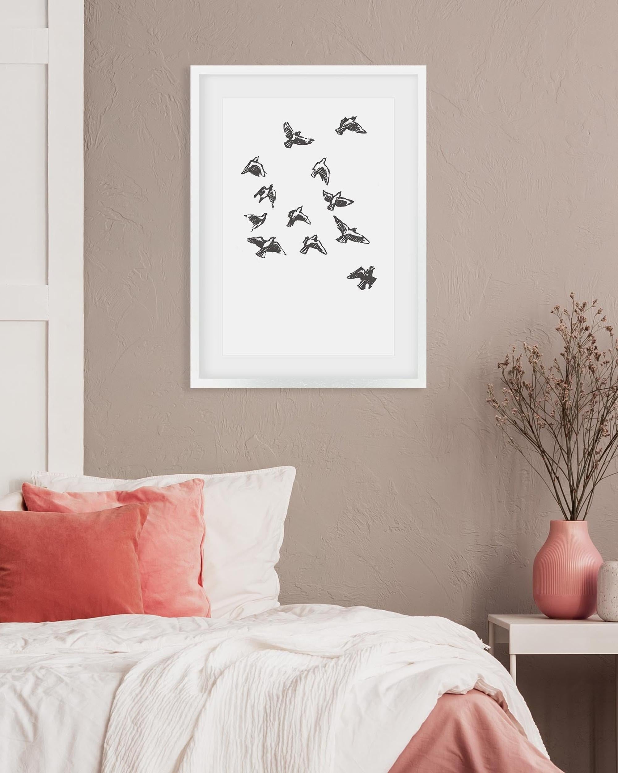 Framed artwork of birds on a wall above a bed with pink and white bedding.