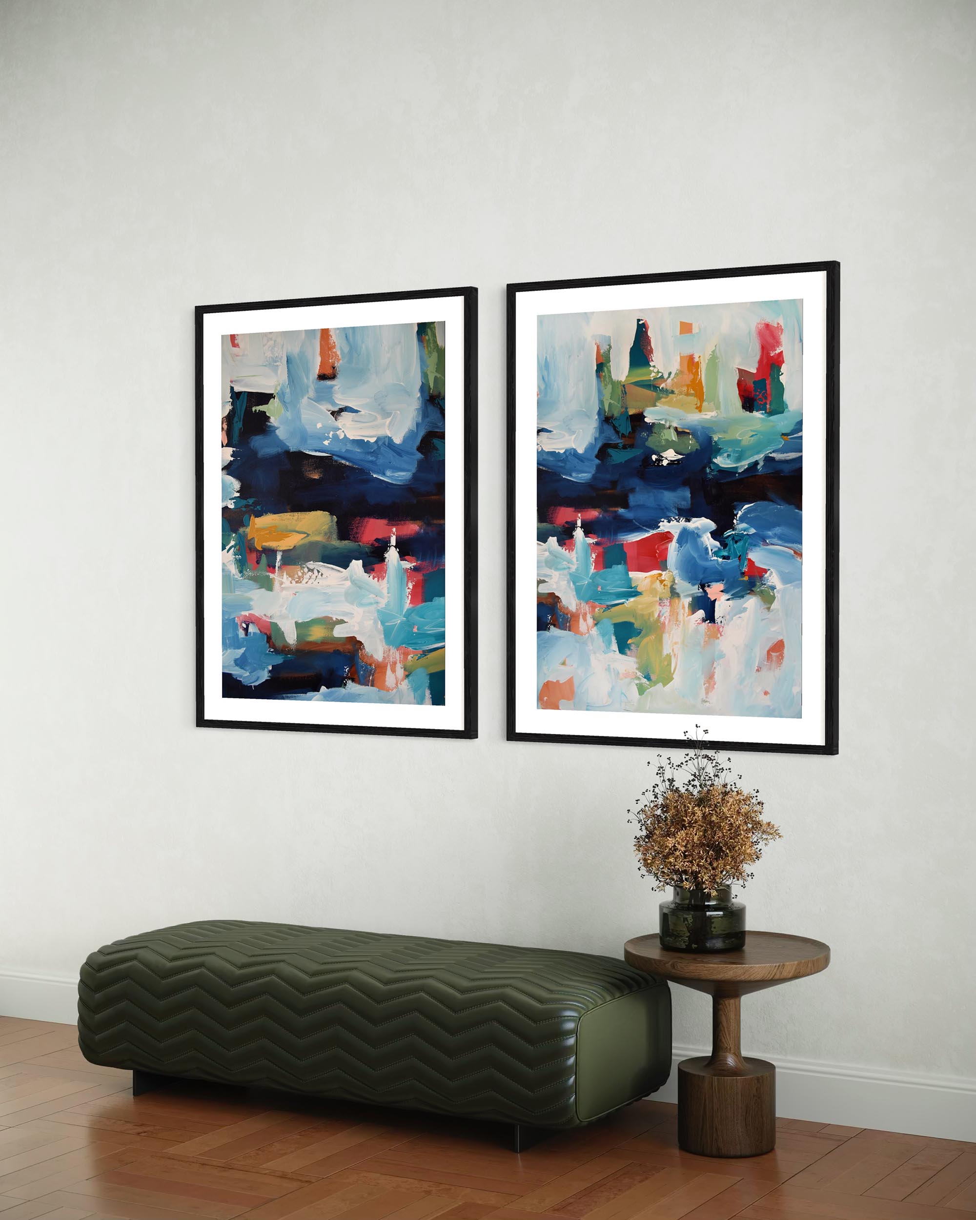 Two abstract art pieces on a wall above a green ottoman and wooden side table.