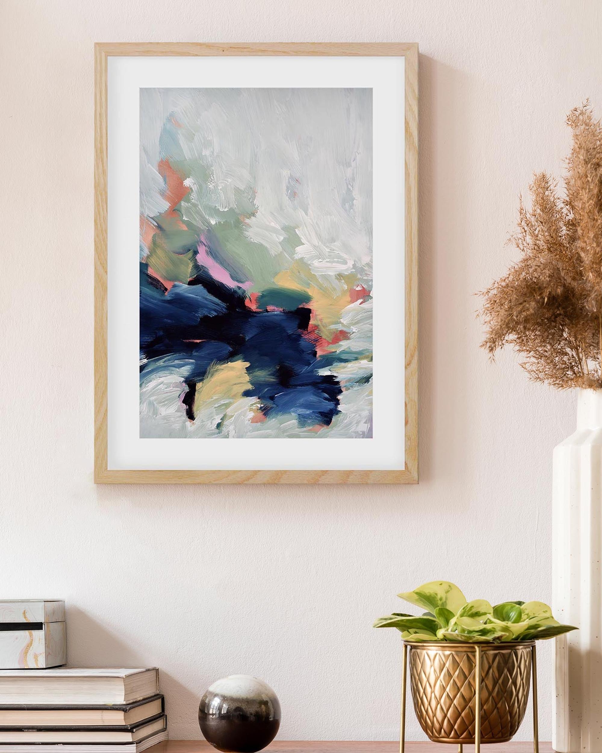 Framed abstract art piece on a wall with decorative vases and plants.