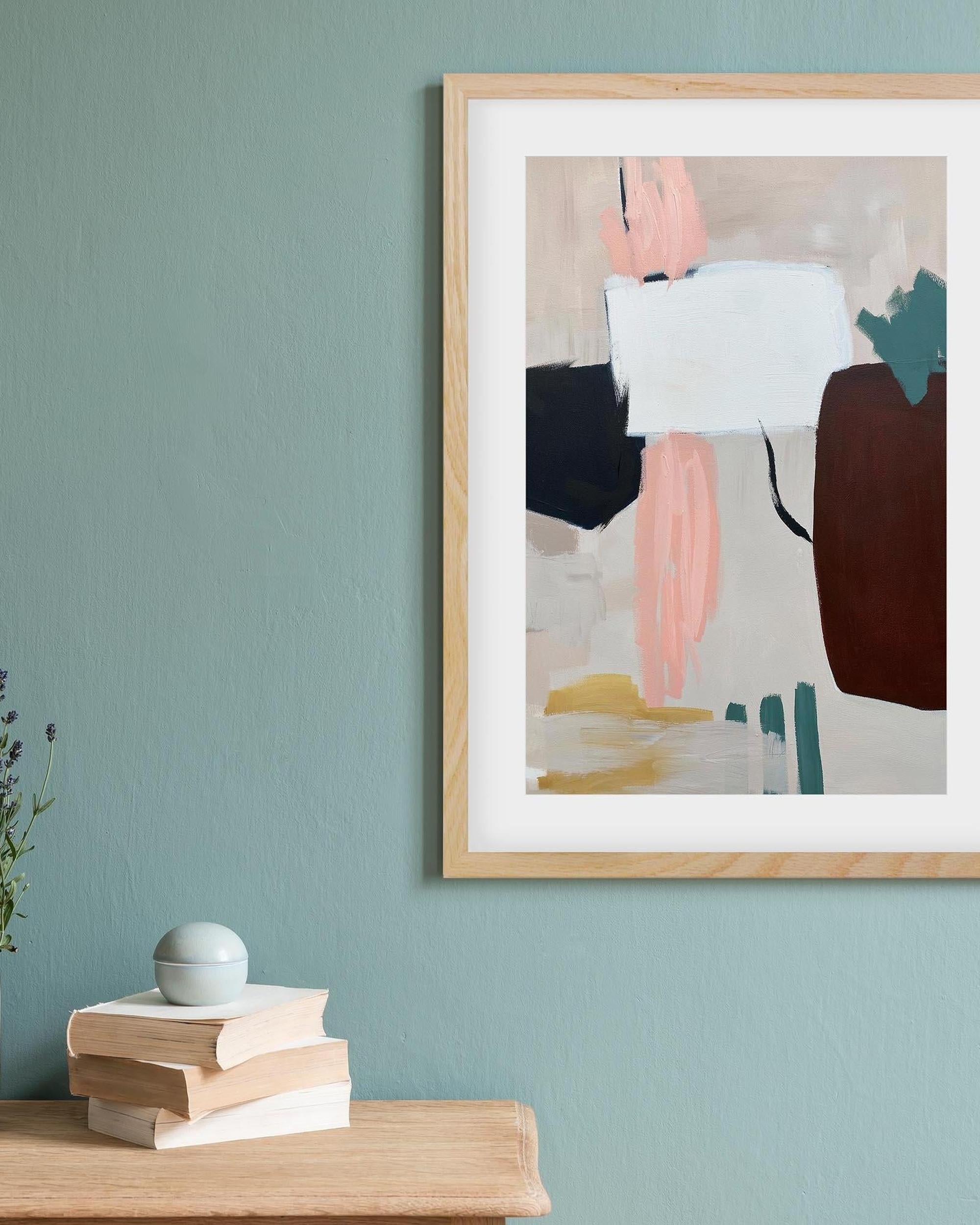 Abstract art print in a wooden frame on a light blue wall with books and a plant below.