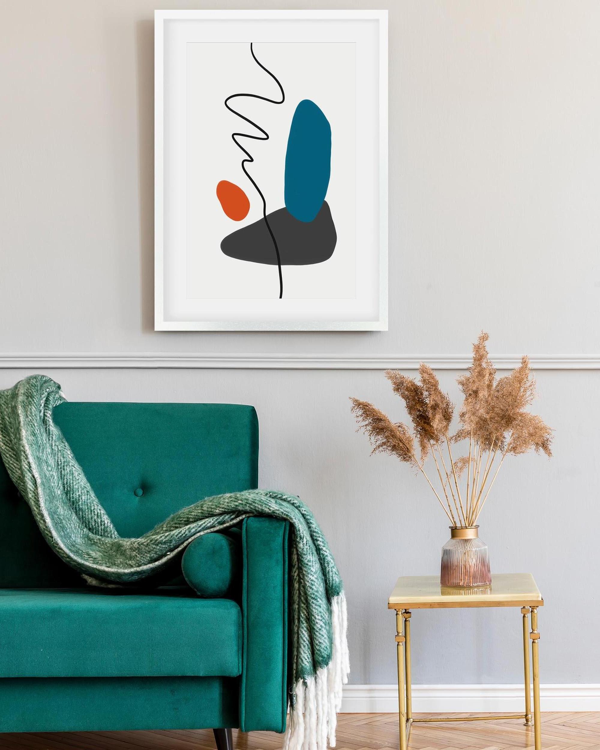 Abstract art print on a wall above a teal armchair with a green blanket.