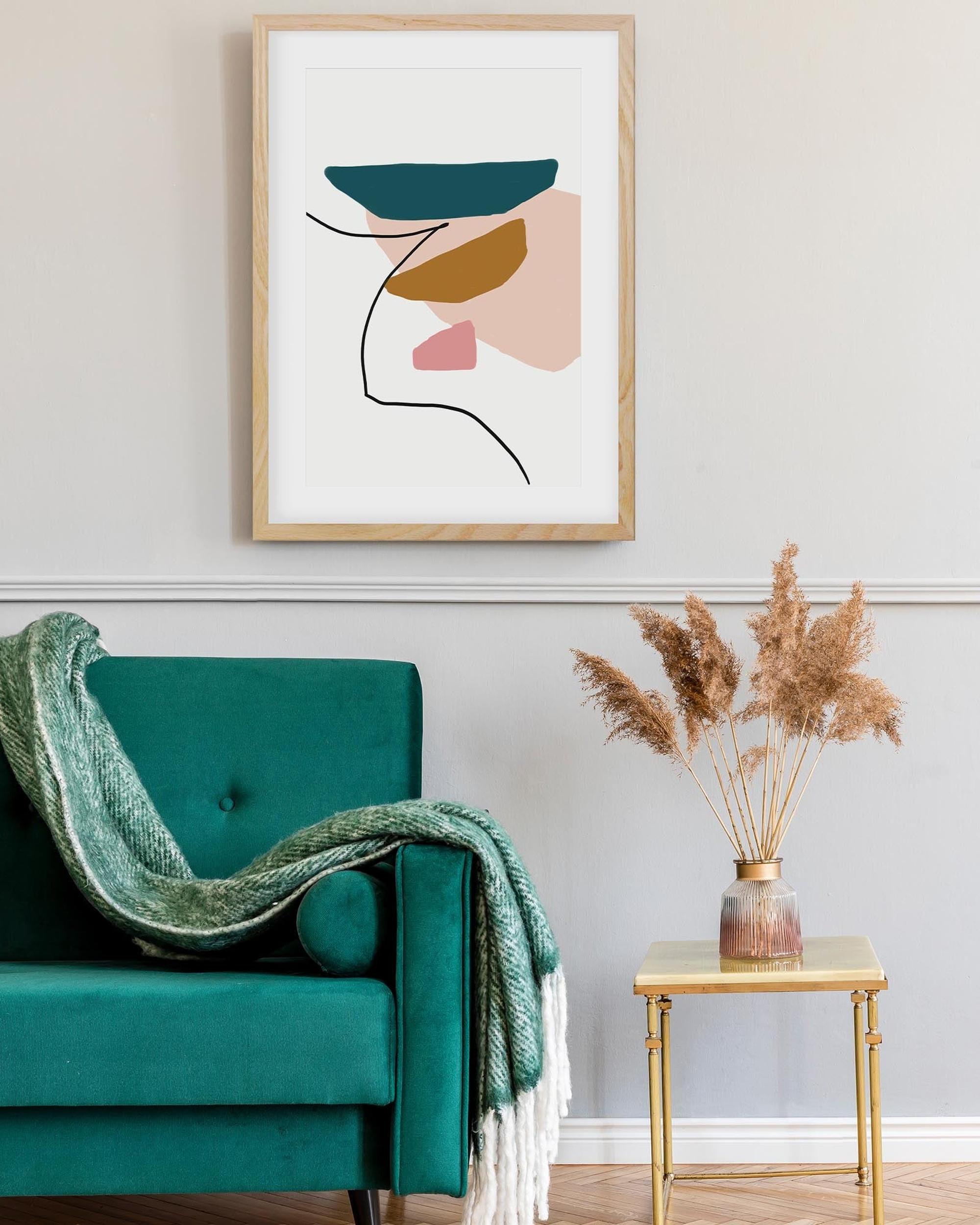Framed abstract art above a teal armchair with a green blanket in a living room setting.
