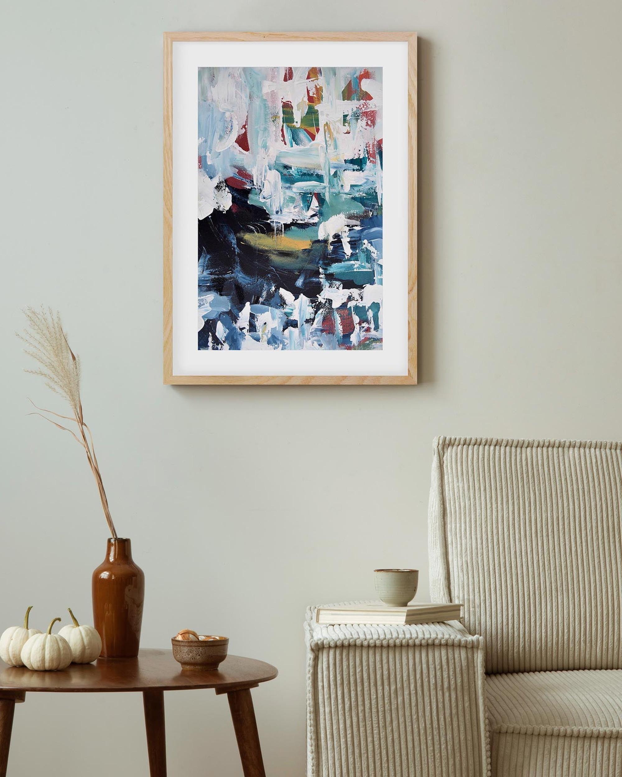 Abstract painting in a wooden frame on a wall above a table with decorative items.