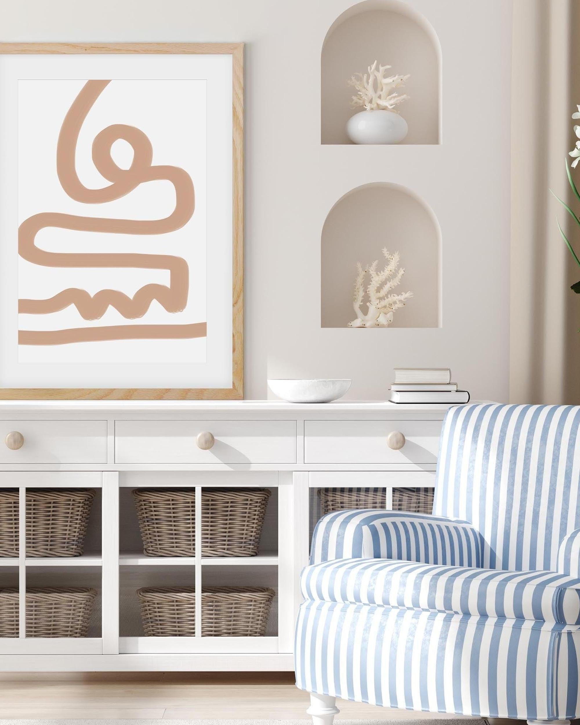 Living room with white wall, framed abstract art, white sideboard with wicker baskets, and blue striped chair.