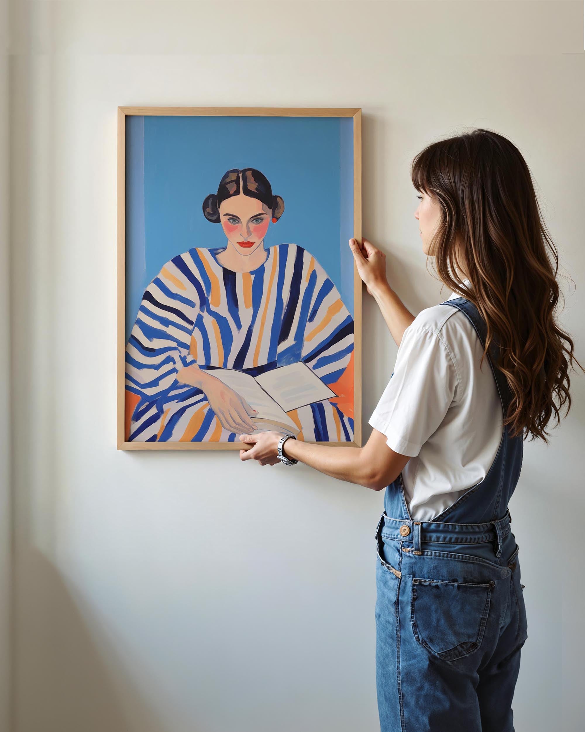 Woman adjusting a framed painting of a woman in a striped dress against a white wall.
