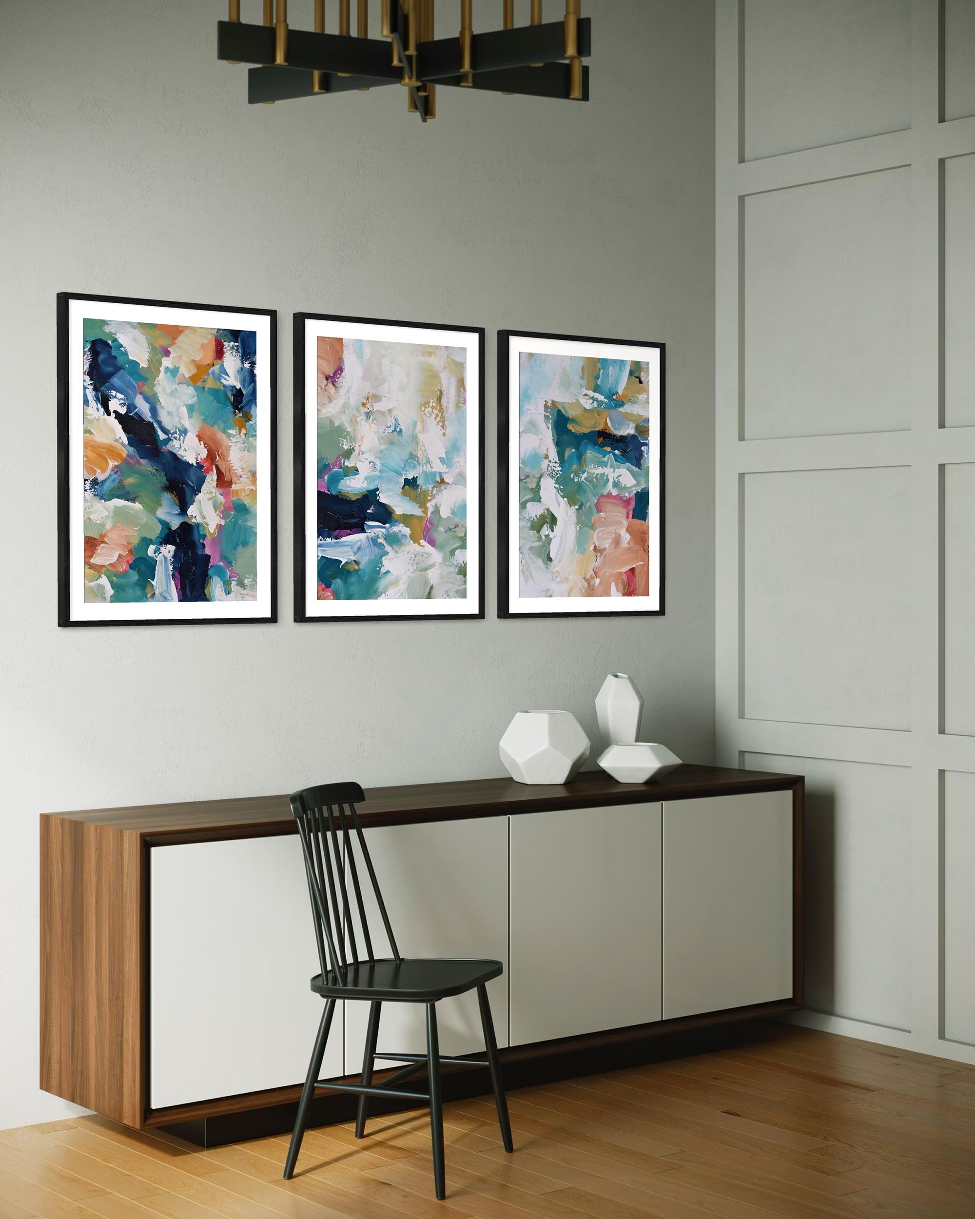 Three abstract paintings on a wall above a console table with a chair.