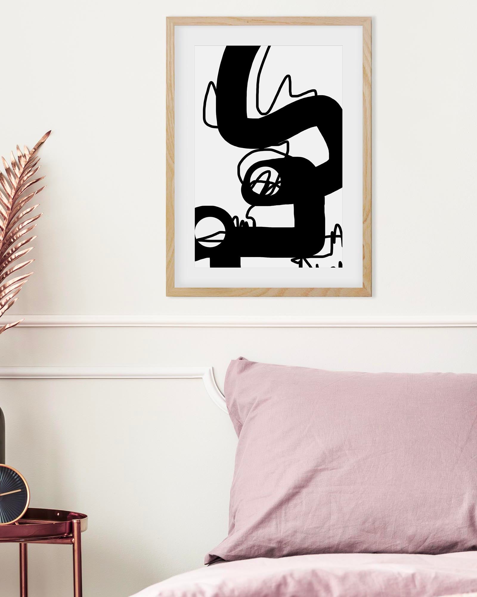 Abstract black and white artwork in a wooden frame on a wall above a bed with pink bedding.