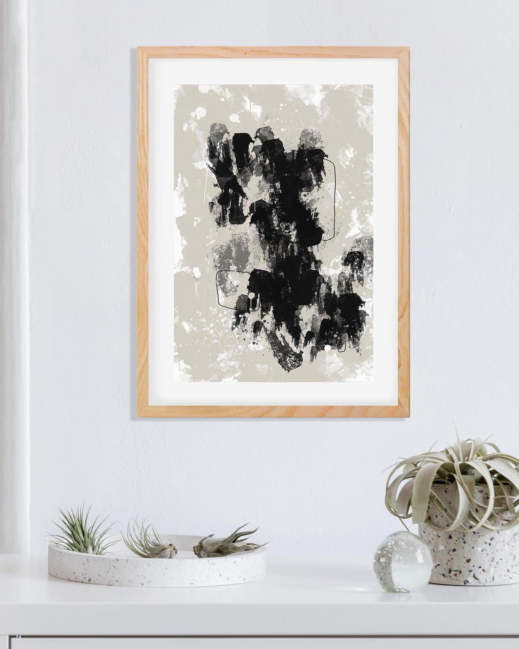 Framed abstract art print on a white wall with decorative plants below.