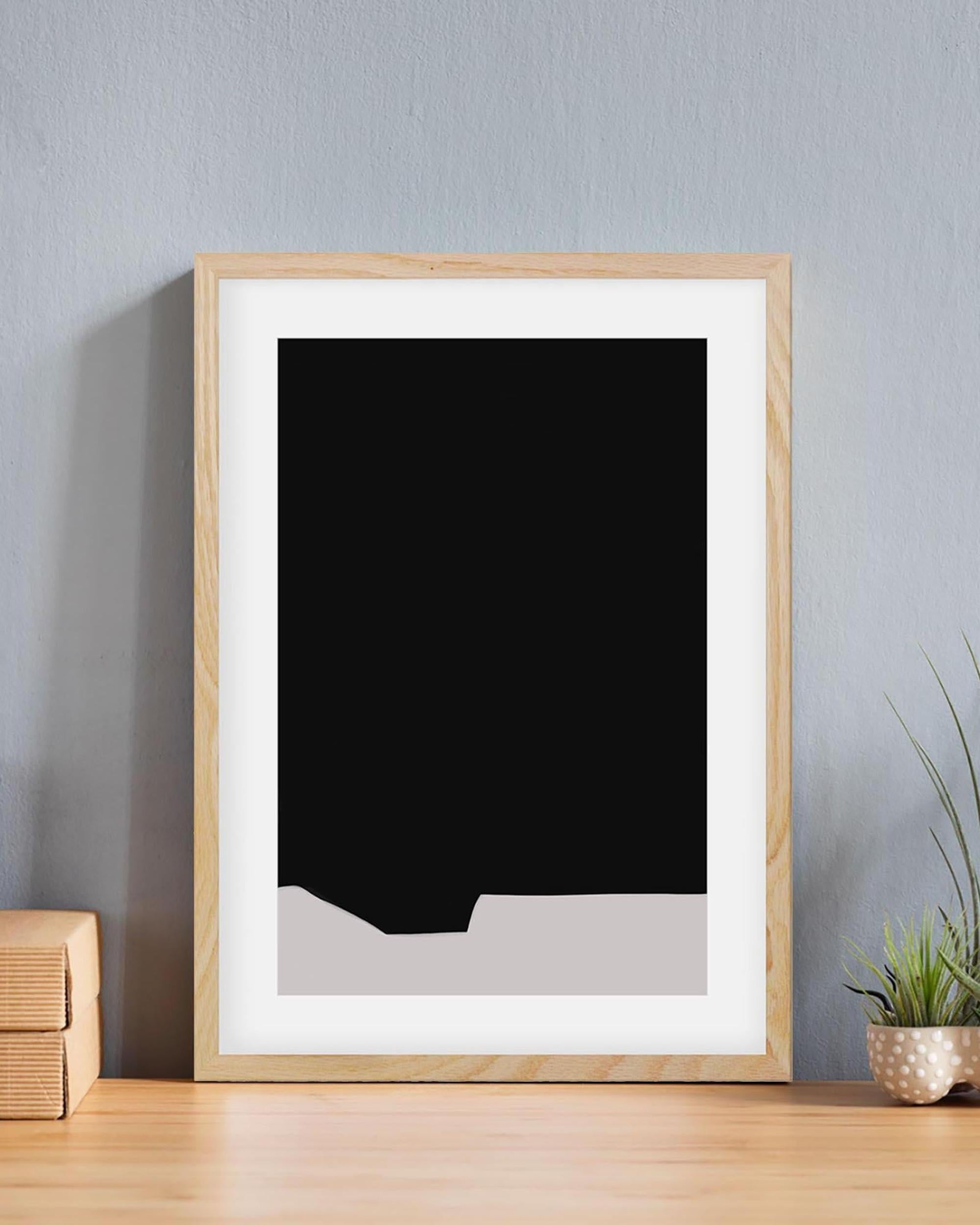 Framed black and white abstract art on a gray wall with a wooden surface and plant.