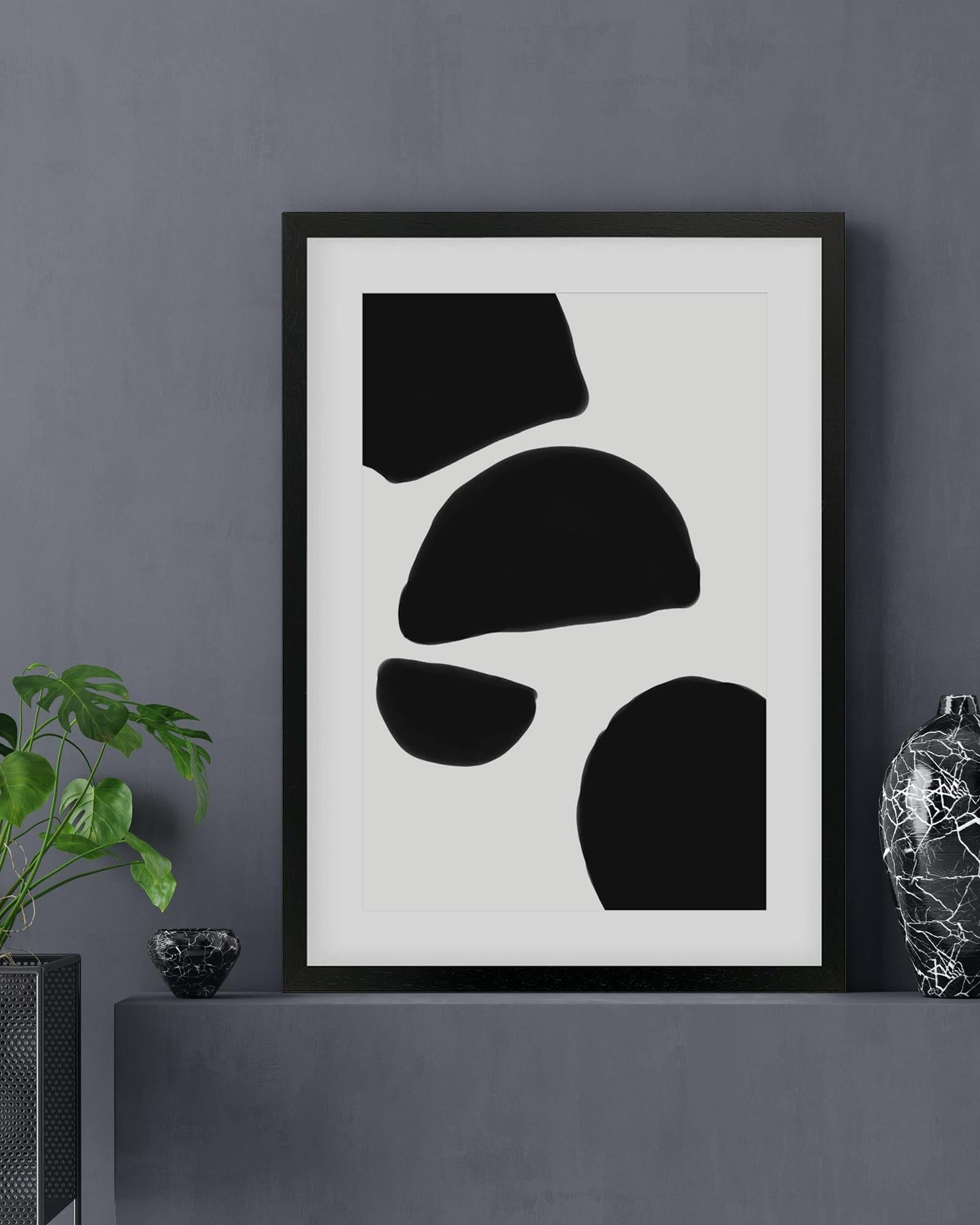 Framed abstract art print with black shapes on a white background, displayed on a gray wall.