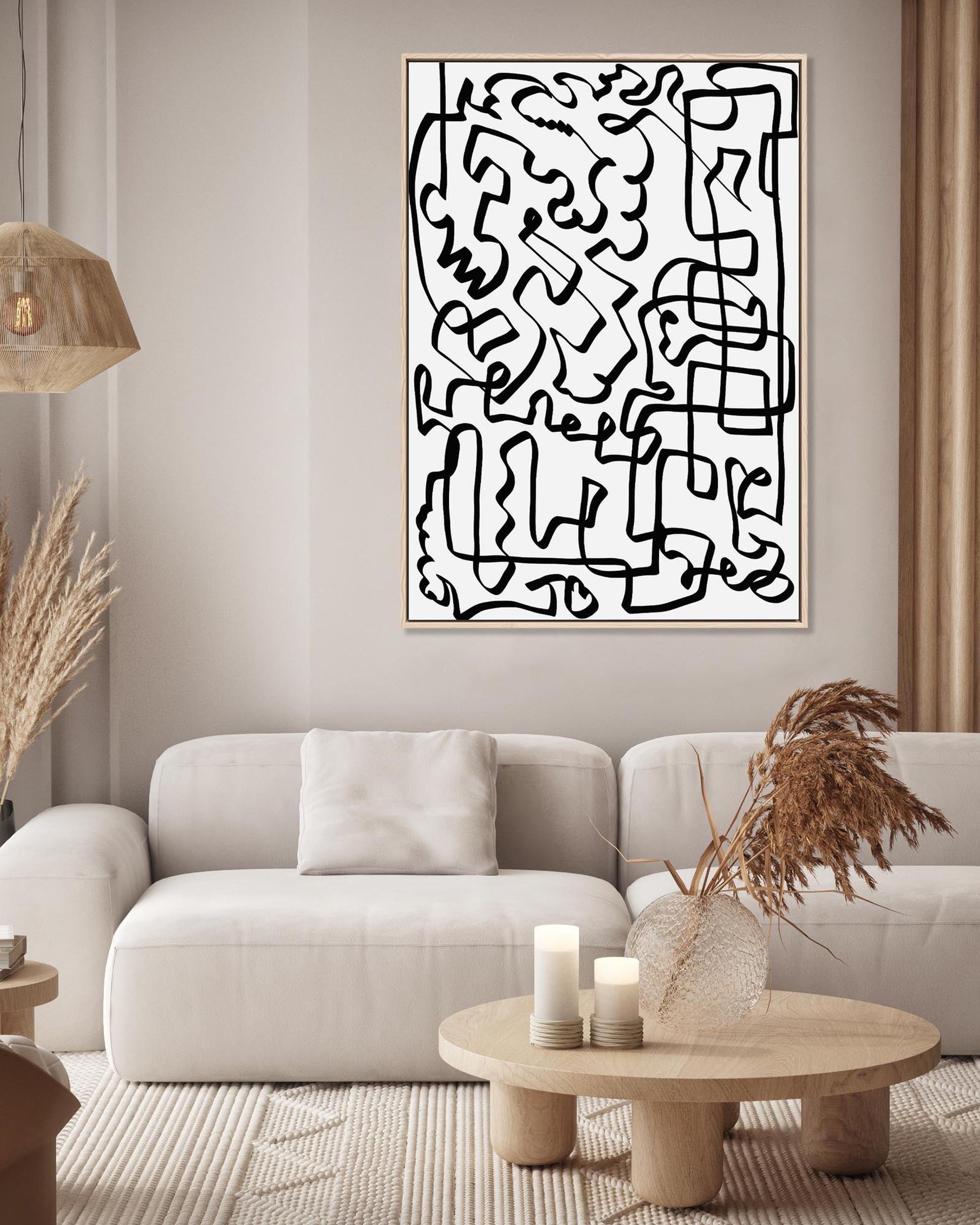 A framed canvas with a black and white line art design displayed above a white sofa and wooden coffee table in a living room setting.