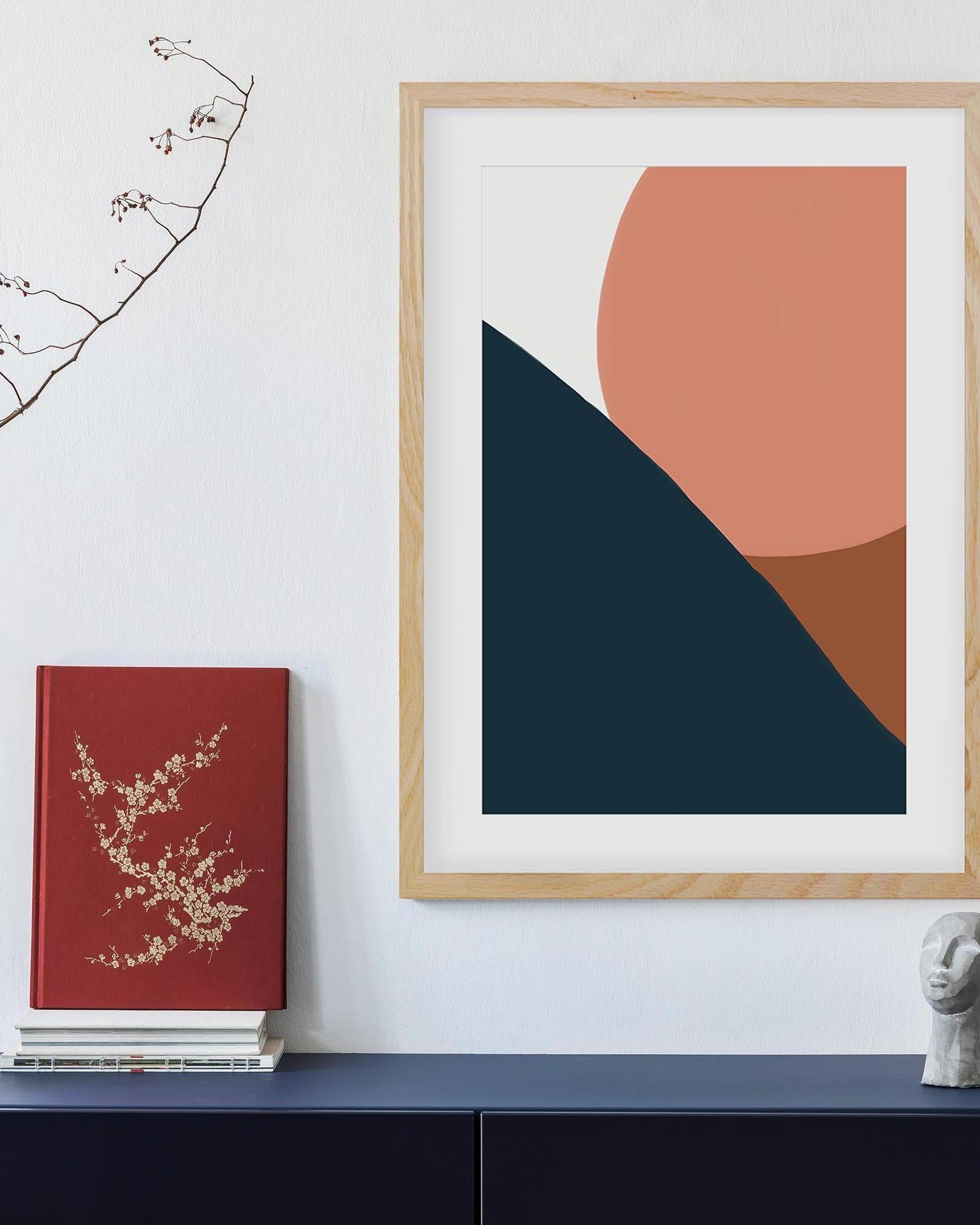 Framed abstract art with geometric shapes on a wall next to a red book.