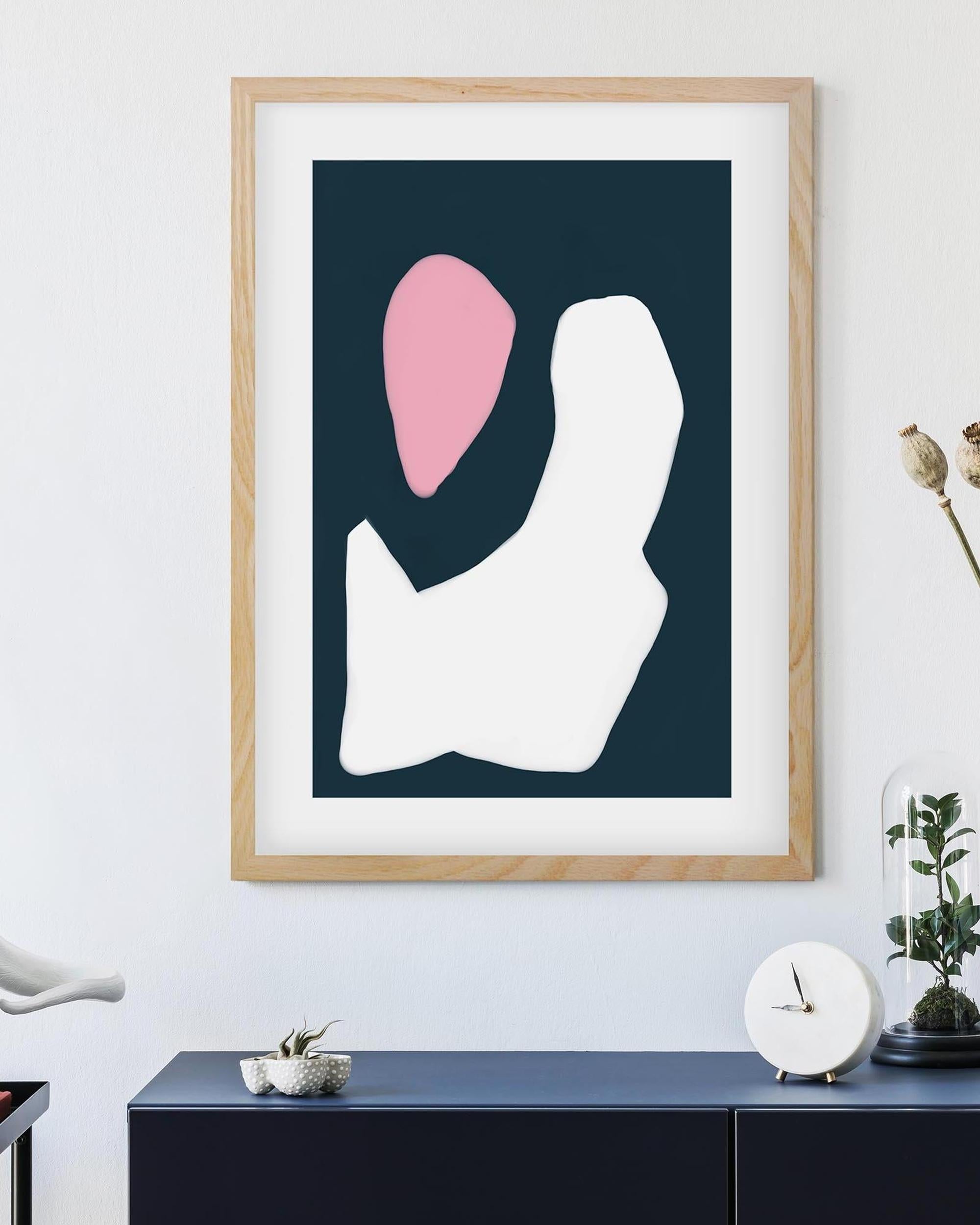 Framed abstract art print with a pink and white shape on a dark blue background, displayed in a room.