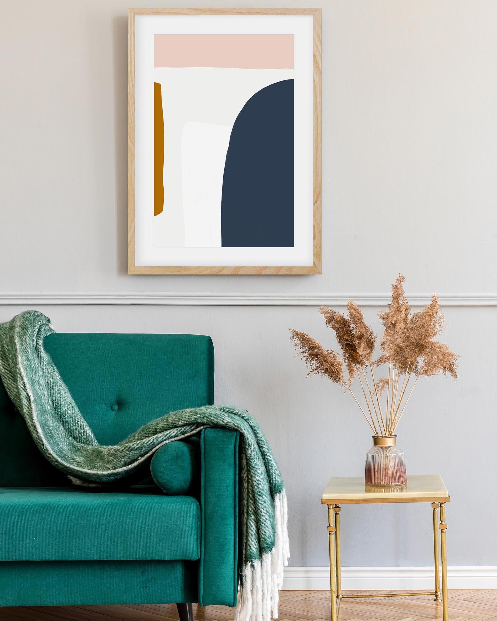 Abstract art print on a wall above a teal armchair with a green blanket.