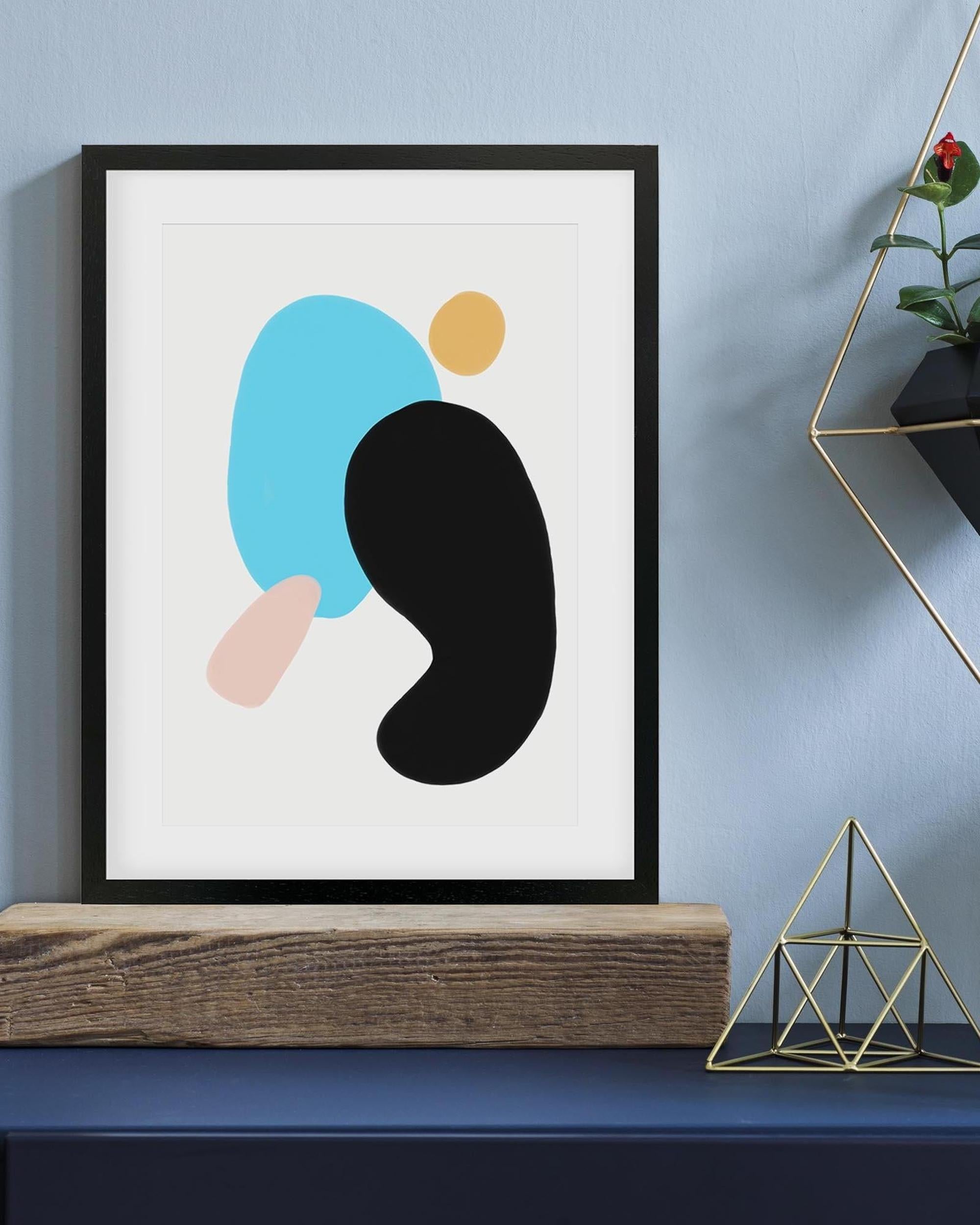 Framed abstract art print with colorful shapes on a blue wall.