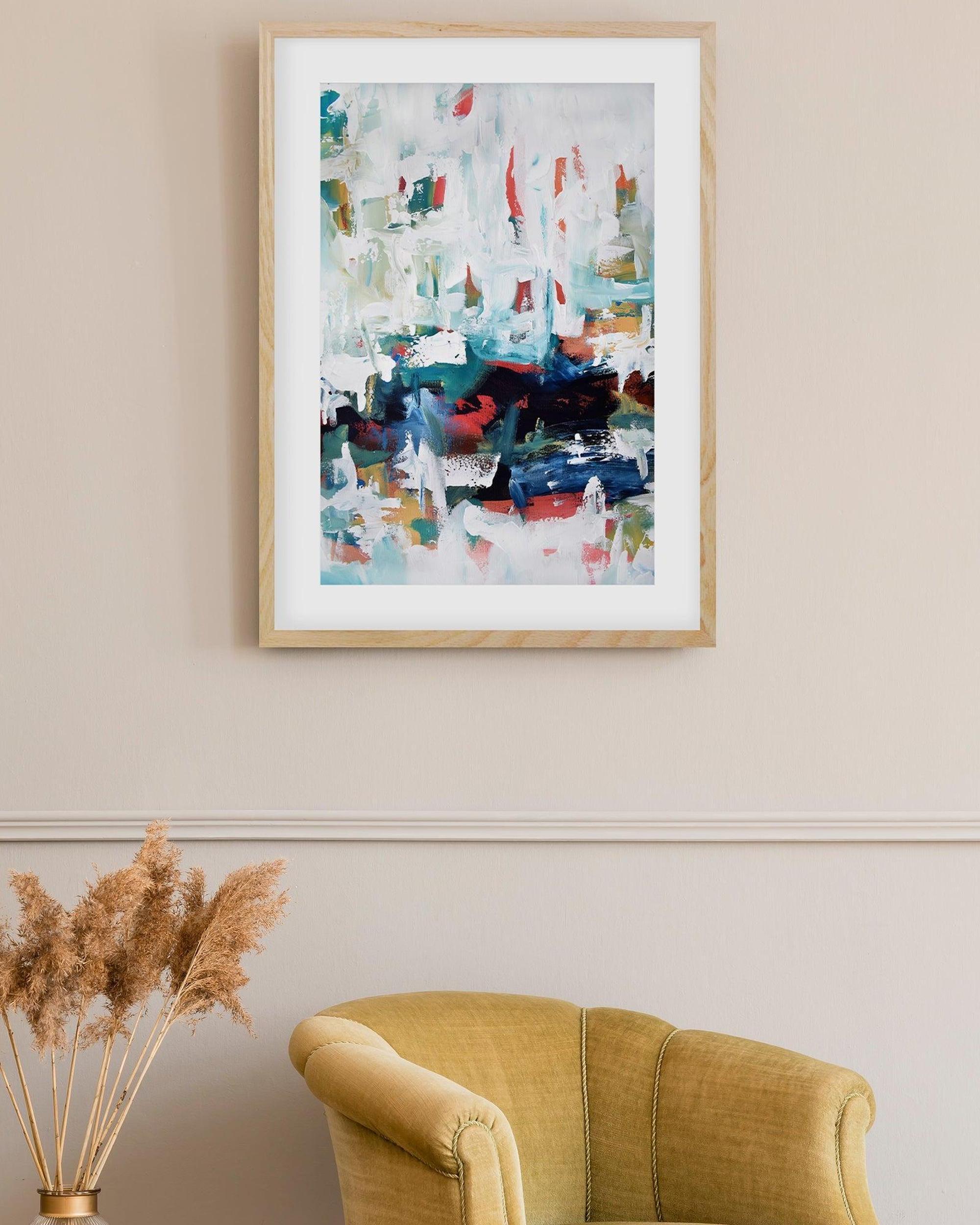 Framed abstract painting on a wall above a yellow armchair with decorative elements.