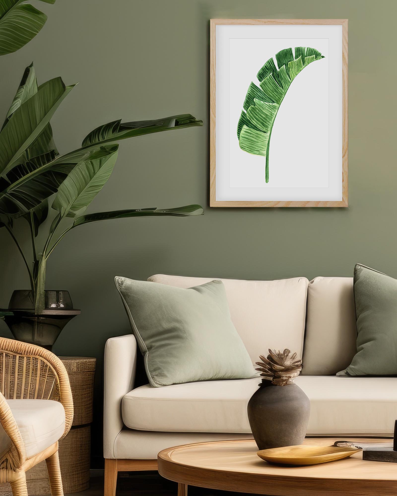 Living room with beige sofa, wicker chair, and framed leaf art on a green wall.