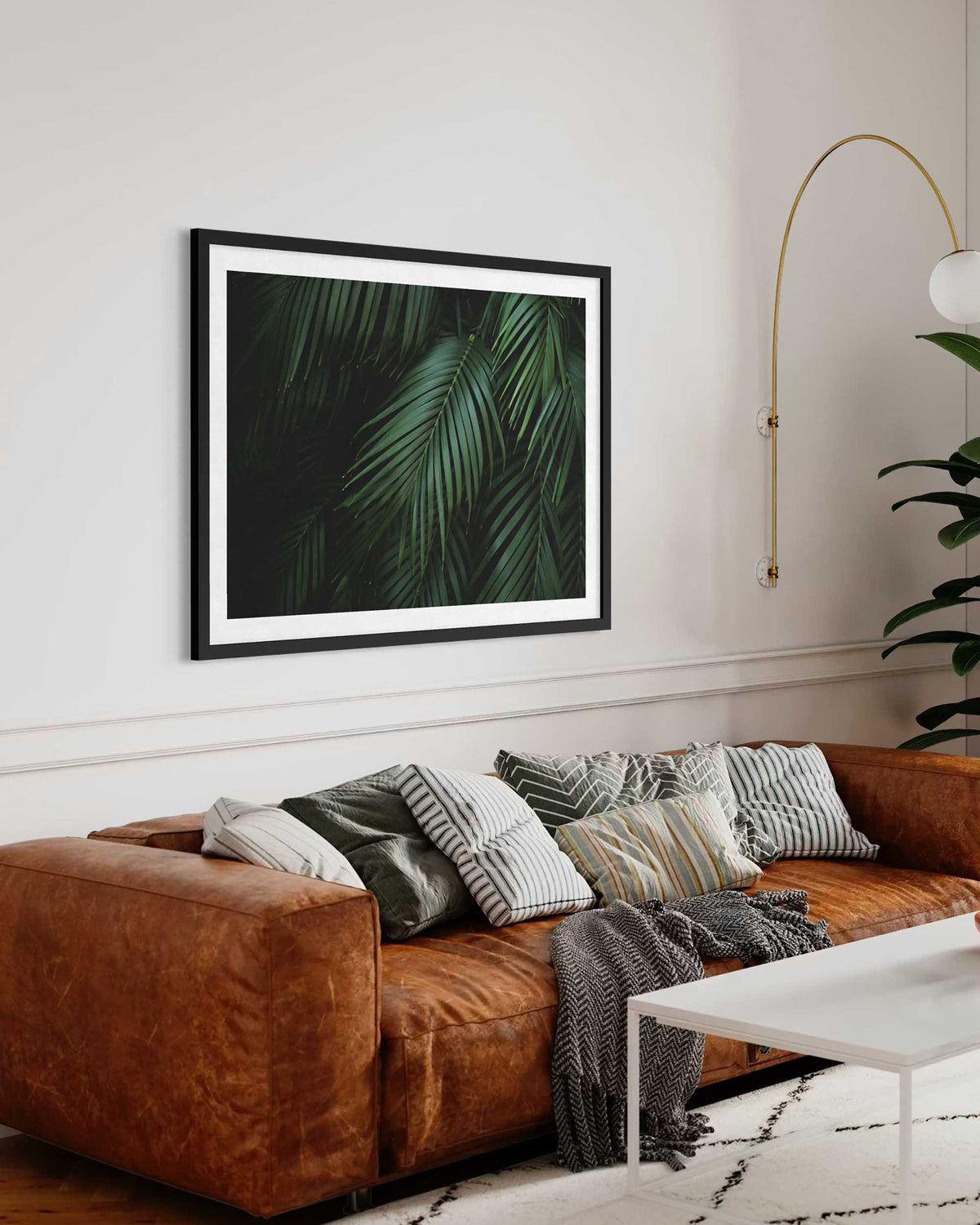 Brown sofa with decorative pillows and a framed leaf print in a living room.