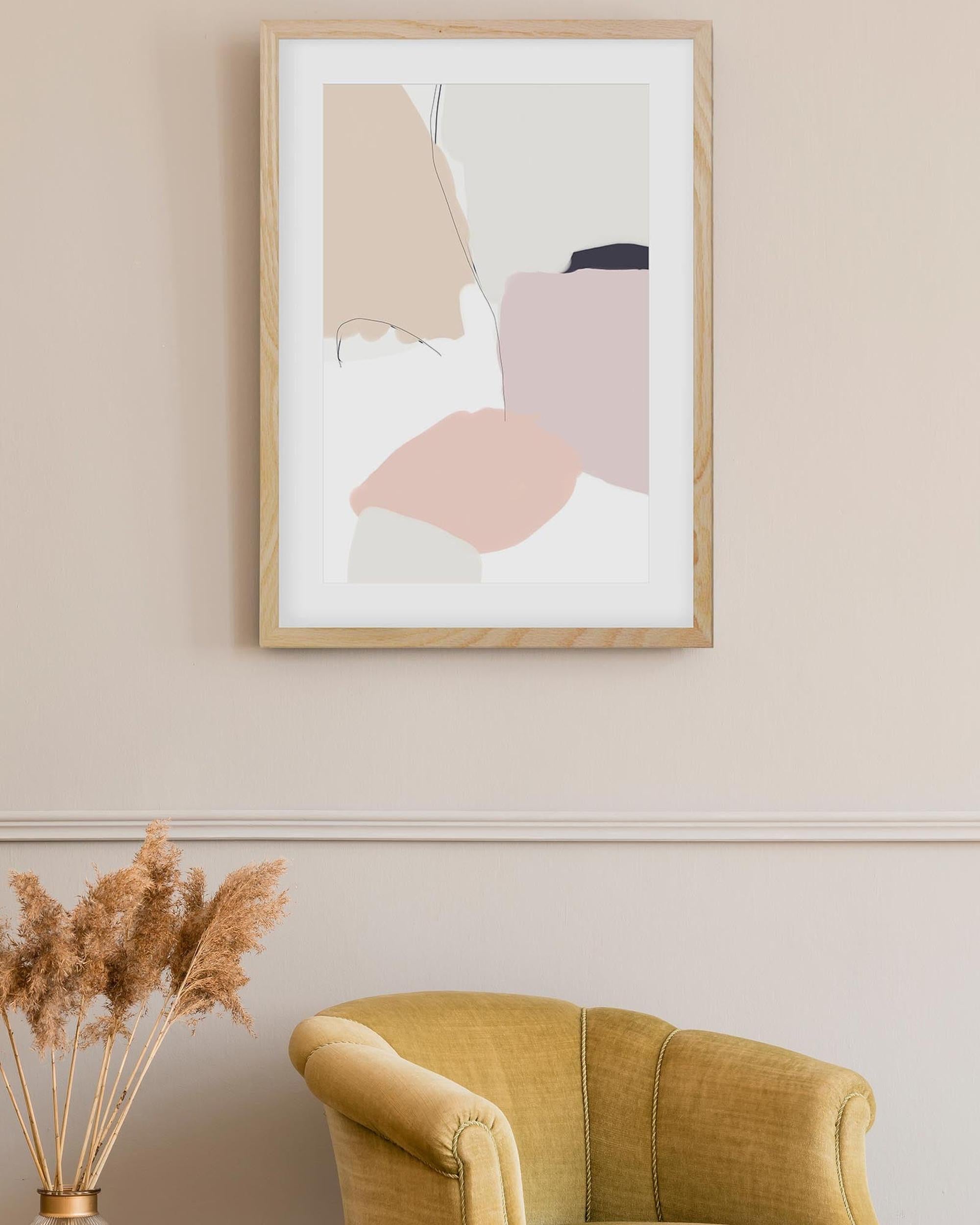 Framed abstract art on a wall above a mustard yellow armchair with dried pampas grass.