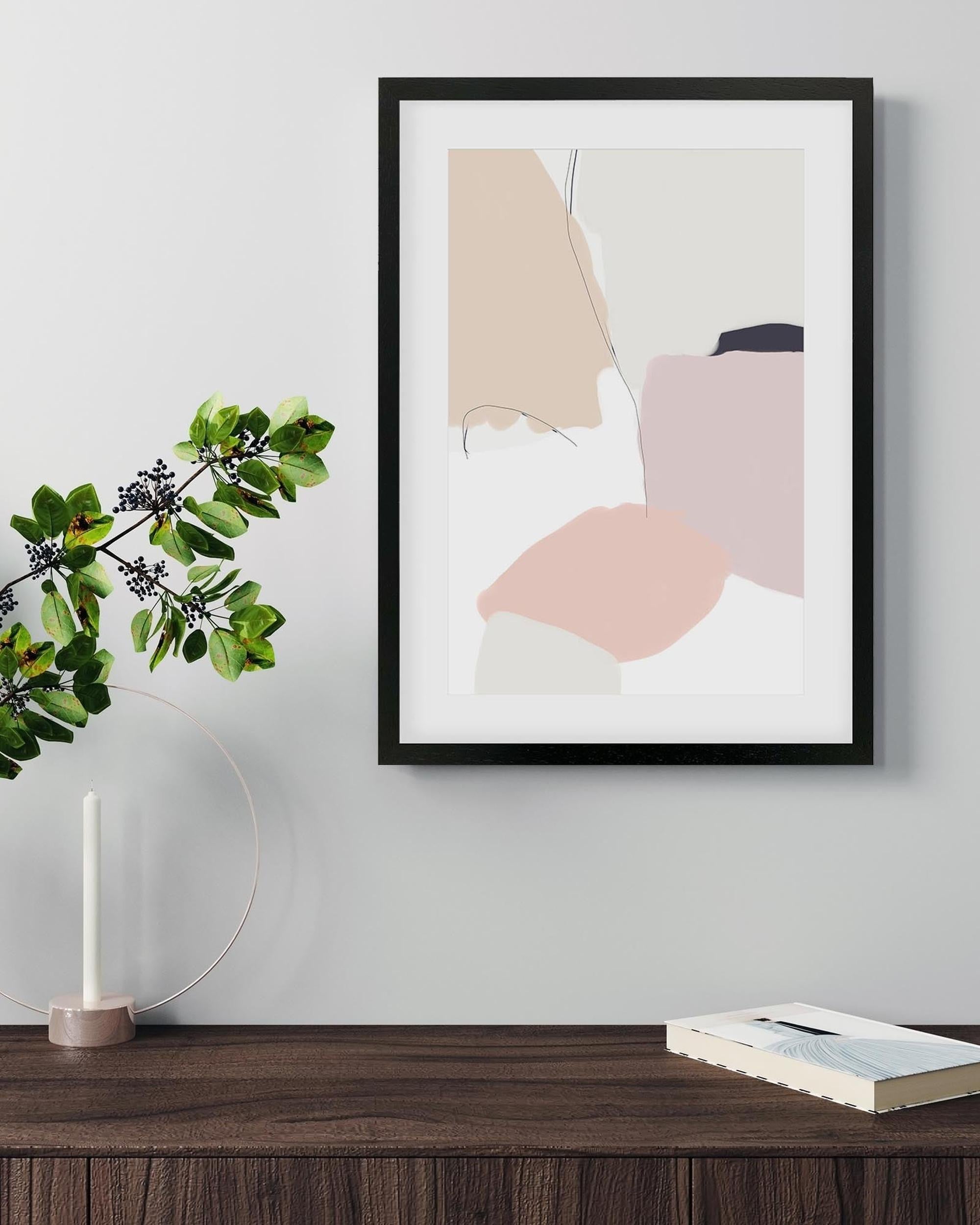 Framed abstract art print on a wall above a wooden surface with a plant and candle.