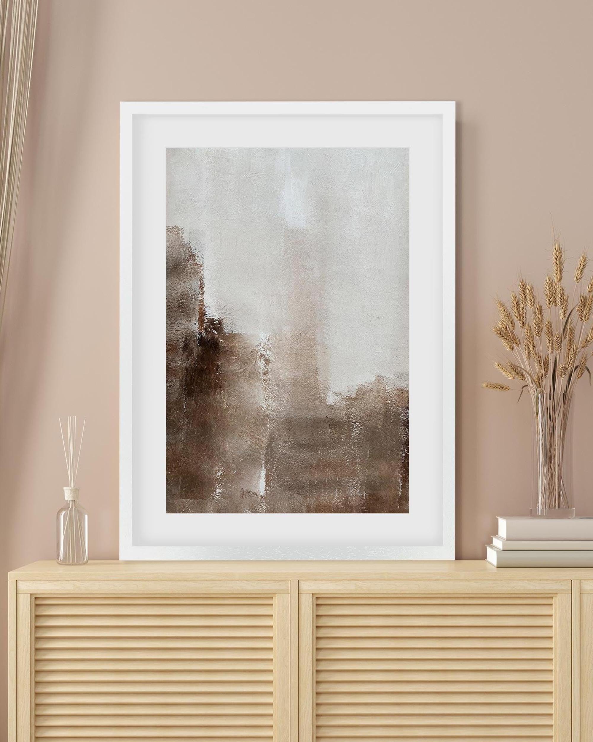 Framed abstract art piece on a beige wall above a wooden cabinet.