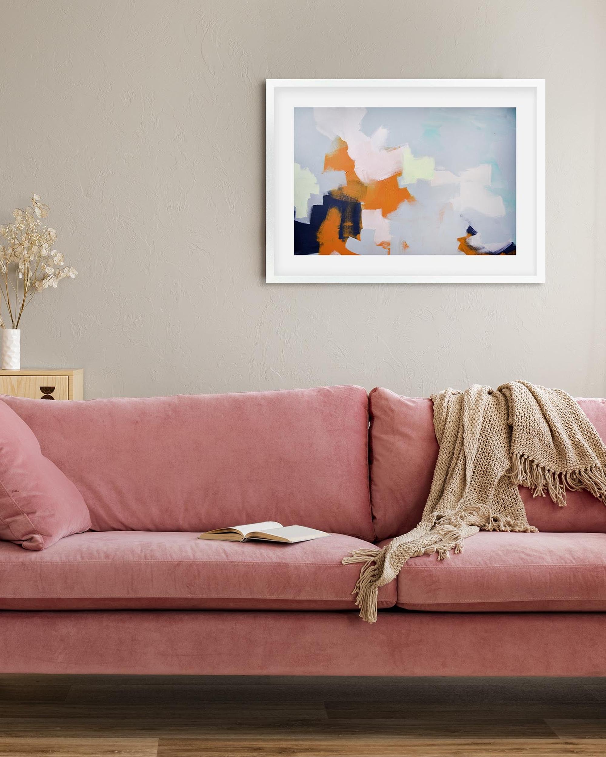 Pink sofa with a blanket and book in a living room with abstract art on the wall.