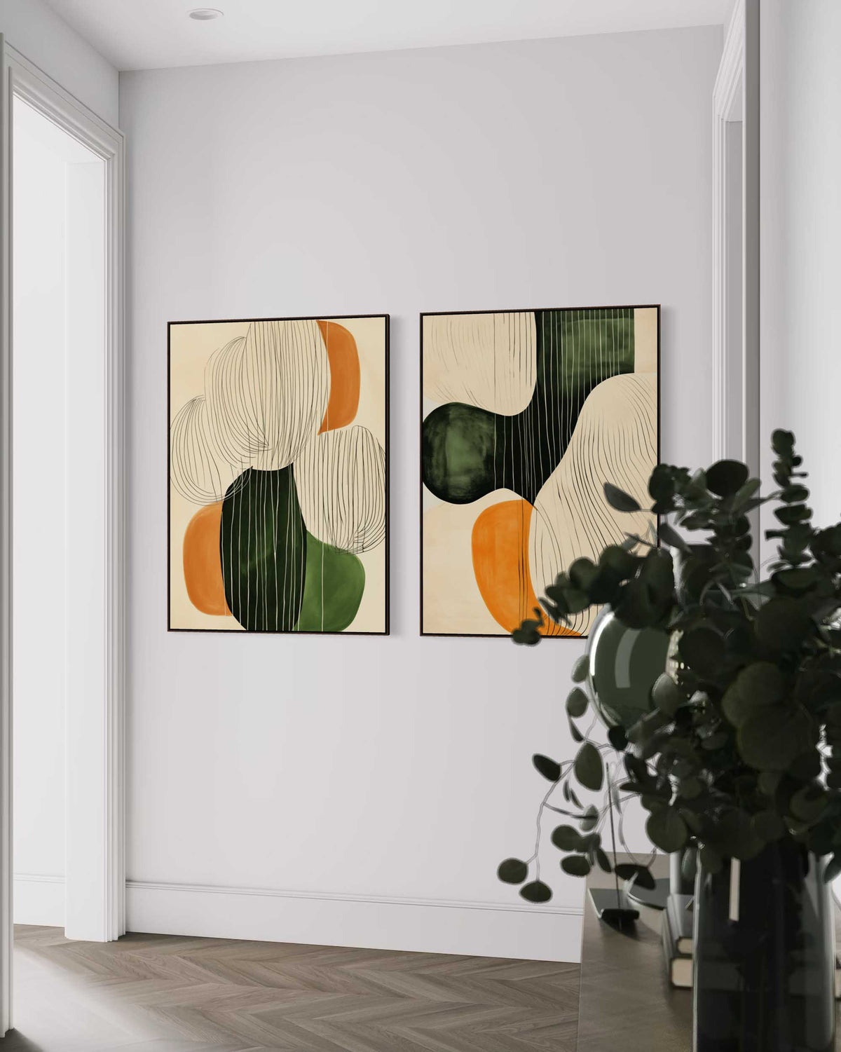 Two abstract art pieces on a wall with a vase of greenery in the foreground.