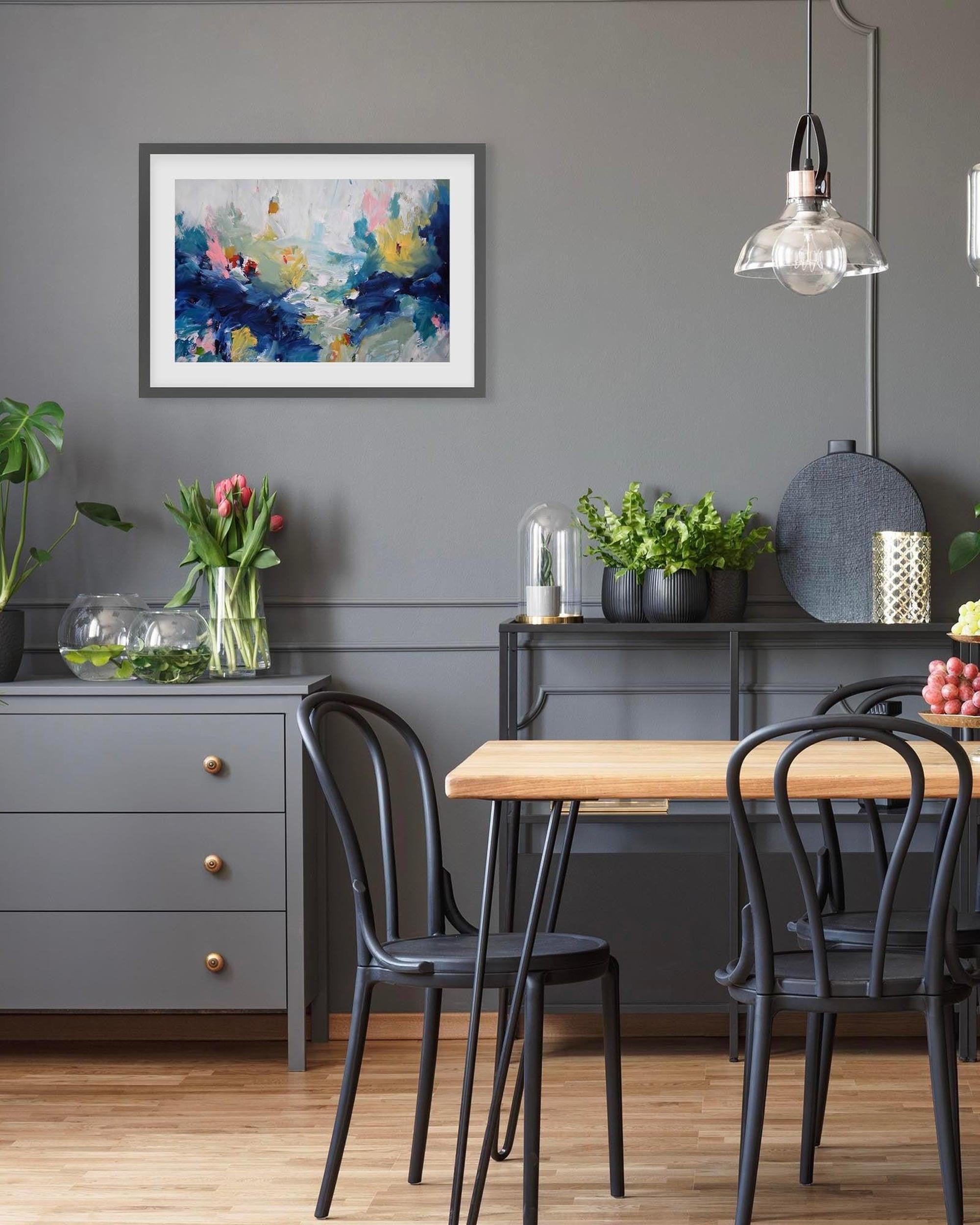 Dining room with a wooden table, black chairs, and a gray wall with a floral painting.