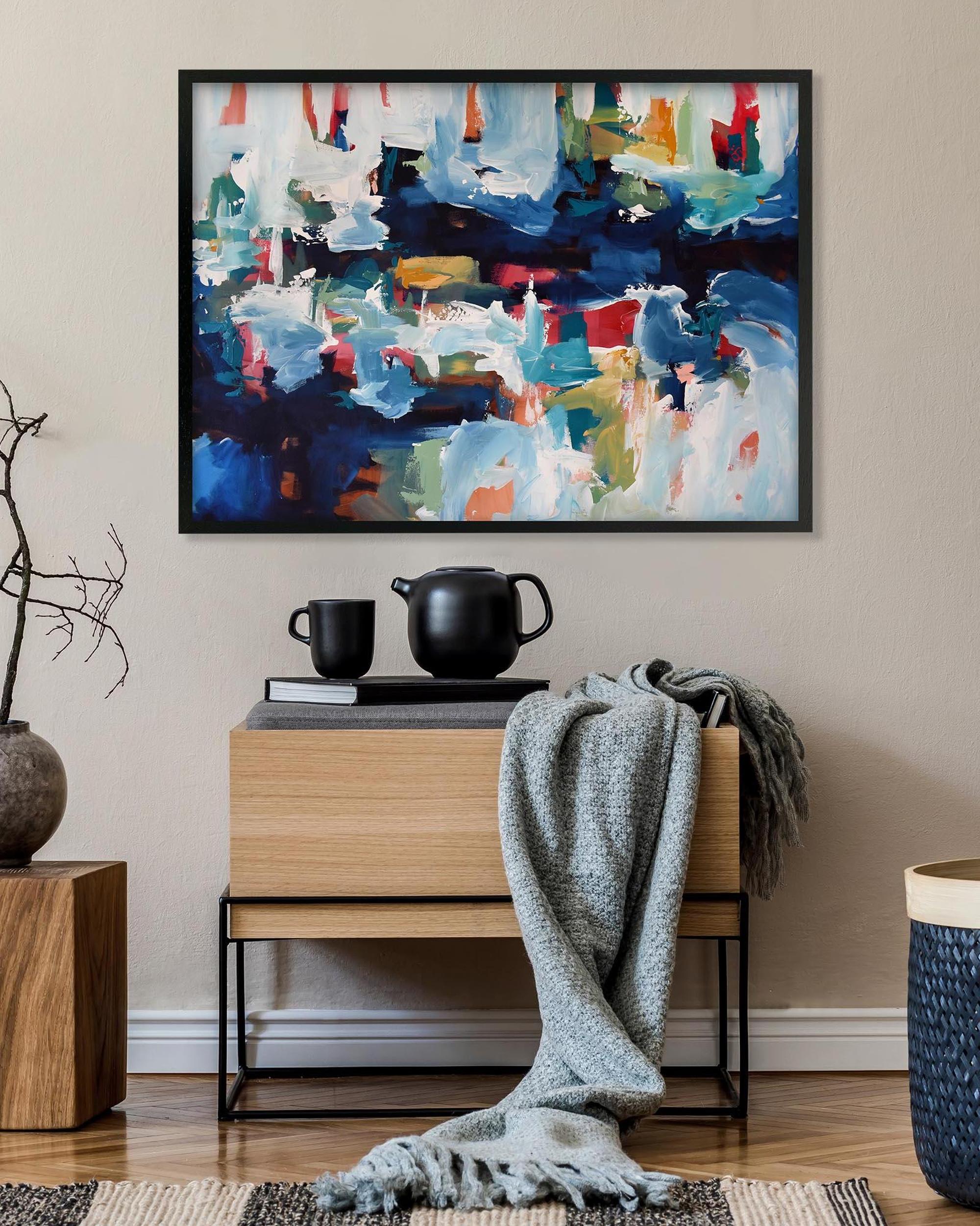 Abstract painting on a wall above a wooden side table with decorative items.